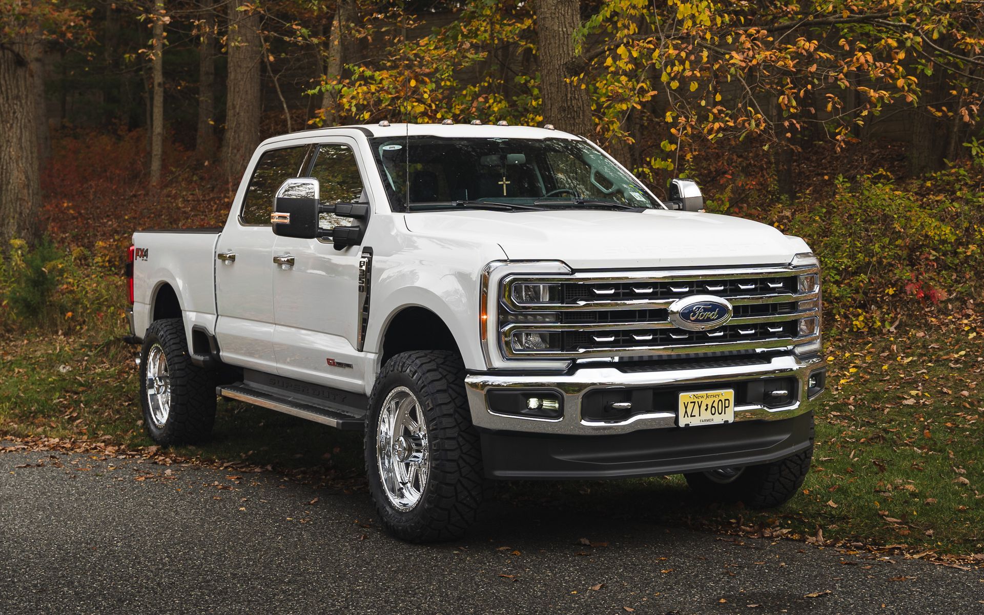 White Ford pickup truck parked on asphalt road, set against a backdrop of trees with fall foliage.