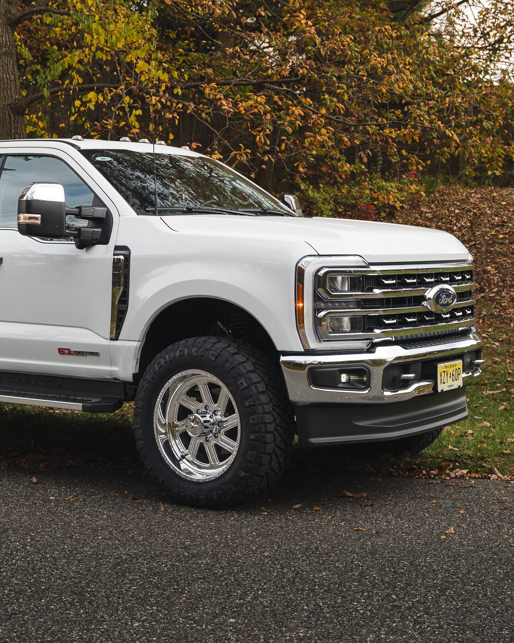 White Ford pickup truck with chrome wheels parked on asphalt, foliage in the background.