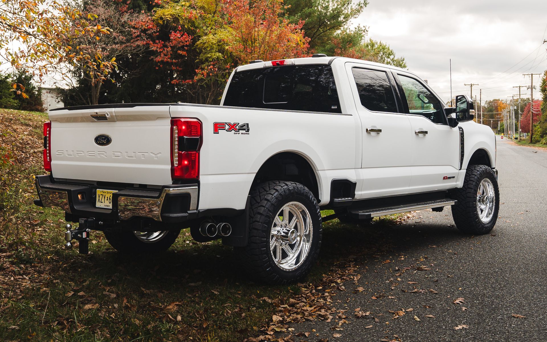 White Ford F-Series pickup truck parked on asphalt road, chrome wheels, Fx4 decal, fall foliage in the background.
