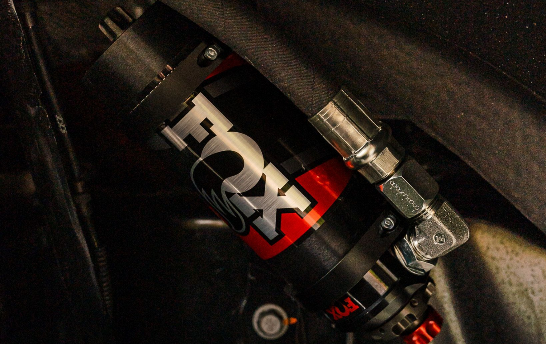 Black and red FOX shock absorber mounted in a vehicle, with silver fittings and hoses.