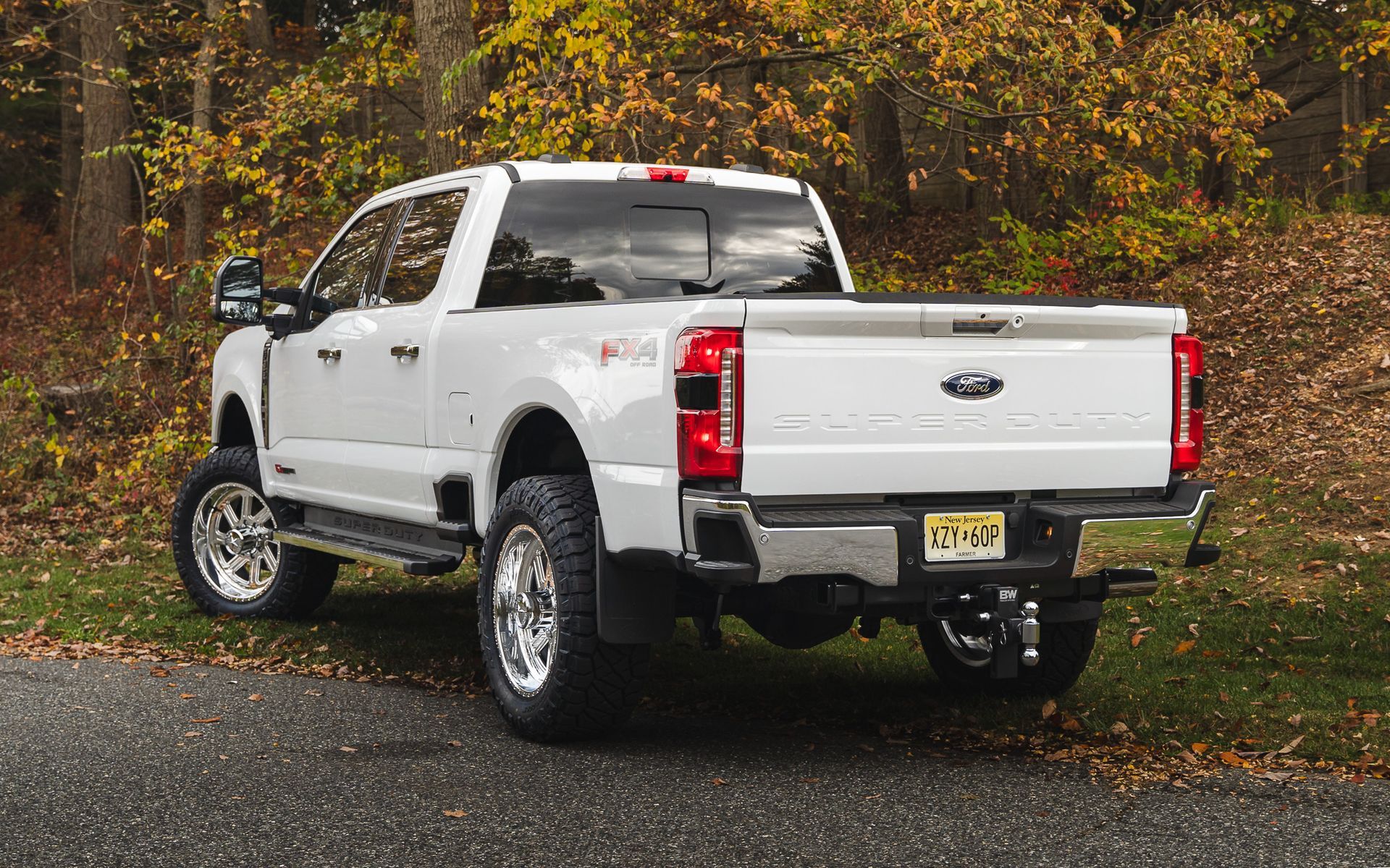 White Ford Super Duty pickup truck parked on a paved road, surrounded by autumn foliage.