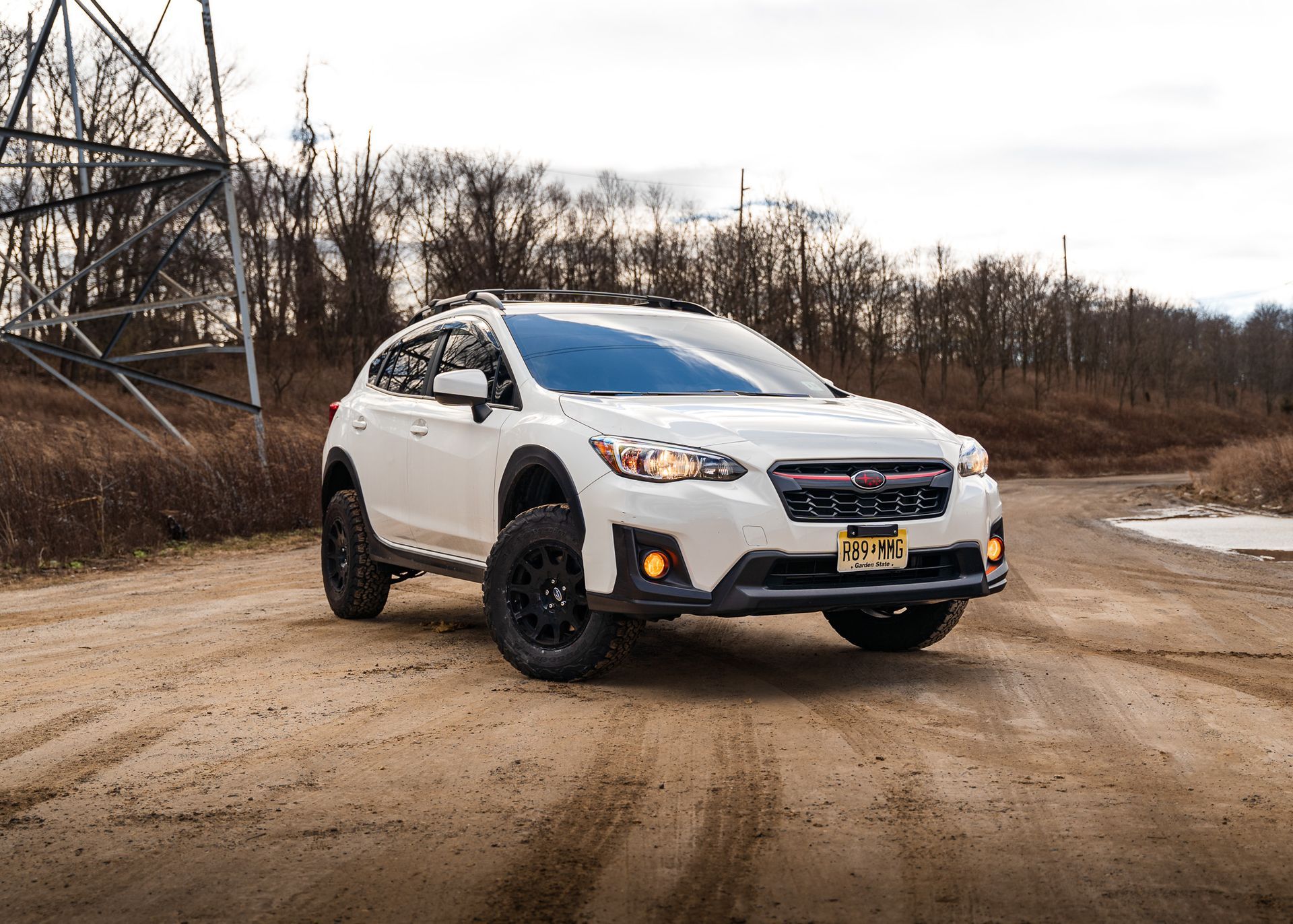 White Subaru Crosstrek on a dirt road with a large power line in the background.