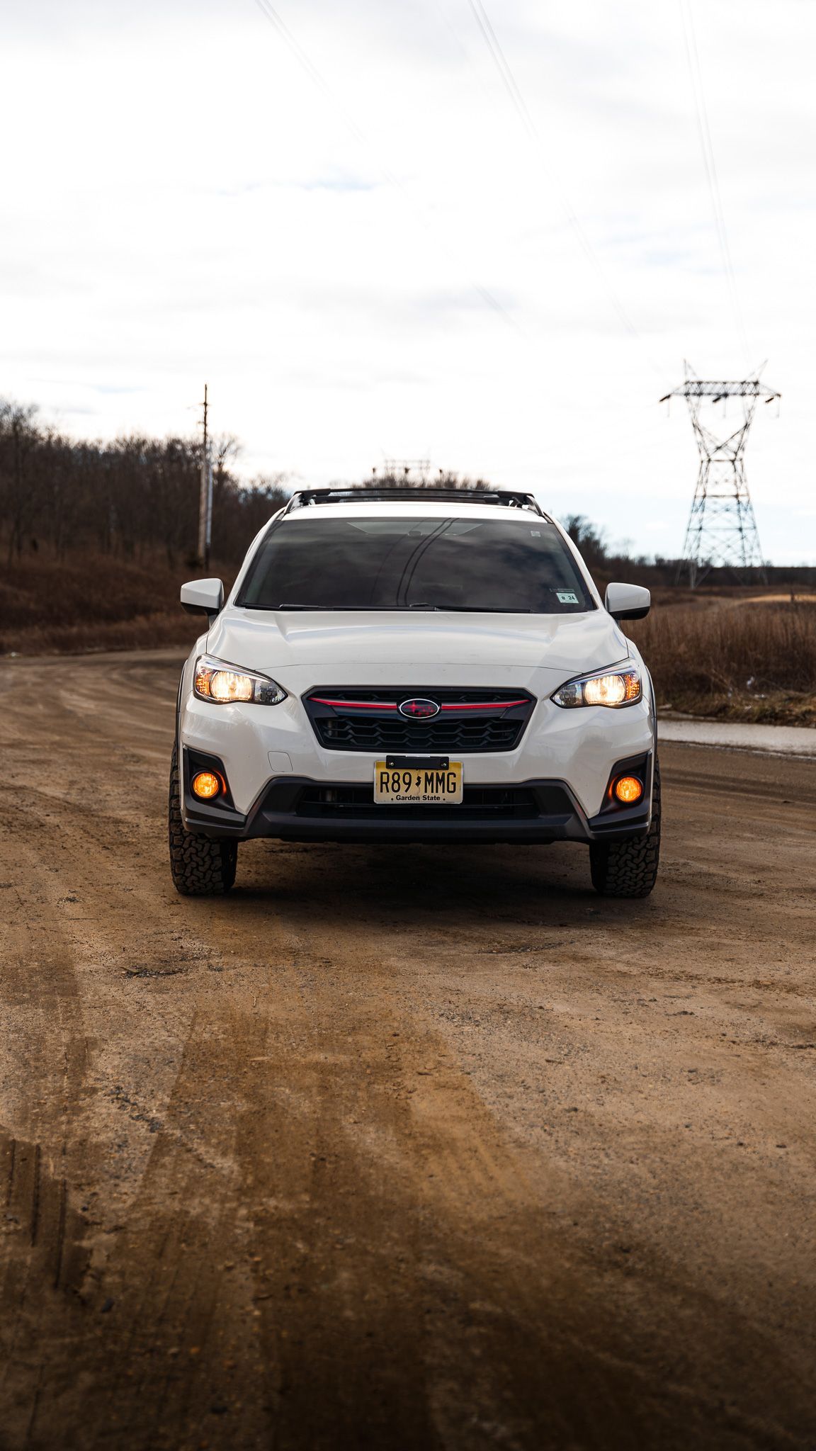 White Subaru SUV on a dirt road, facing the camera with a utility tower in the background.