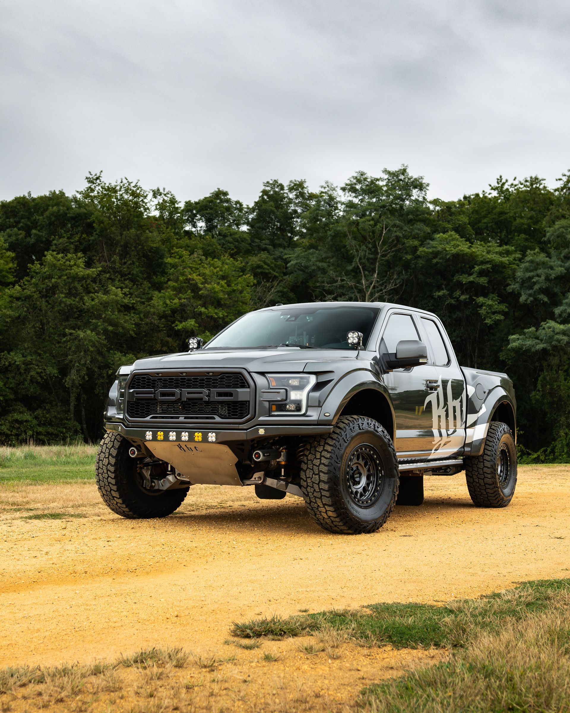 Gray Ford Raptor truck, front view, illuminated headlights and running lights, parked at night.