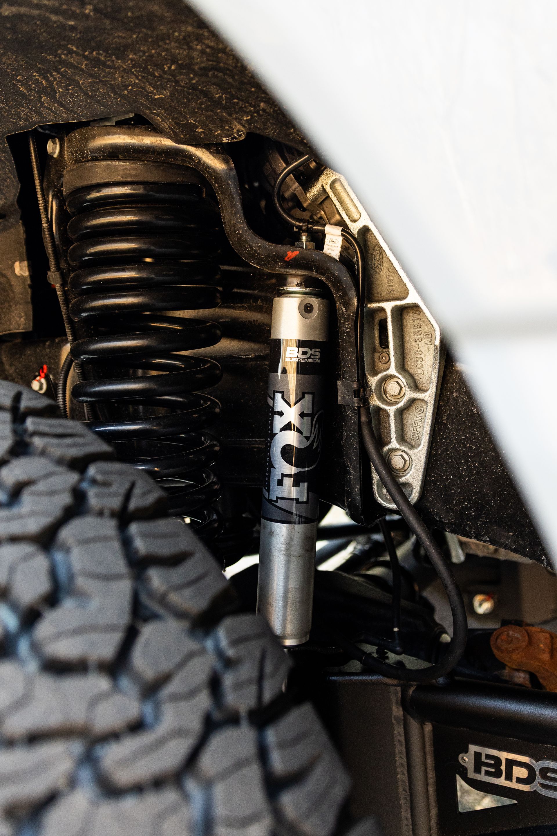 A close-up of a Fox suspension shock absorber mounted on a black coil spring in a vehicle's wheel well.