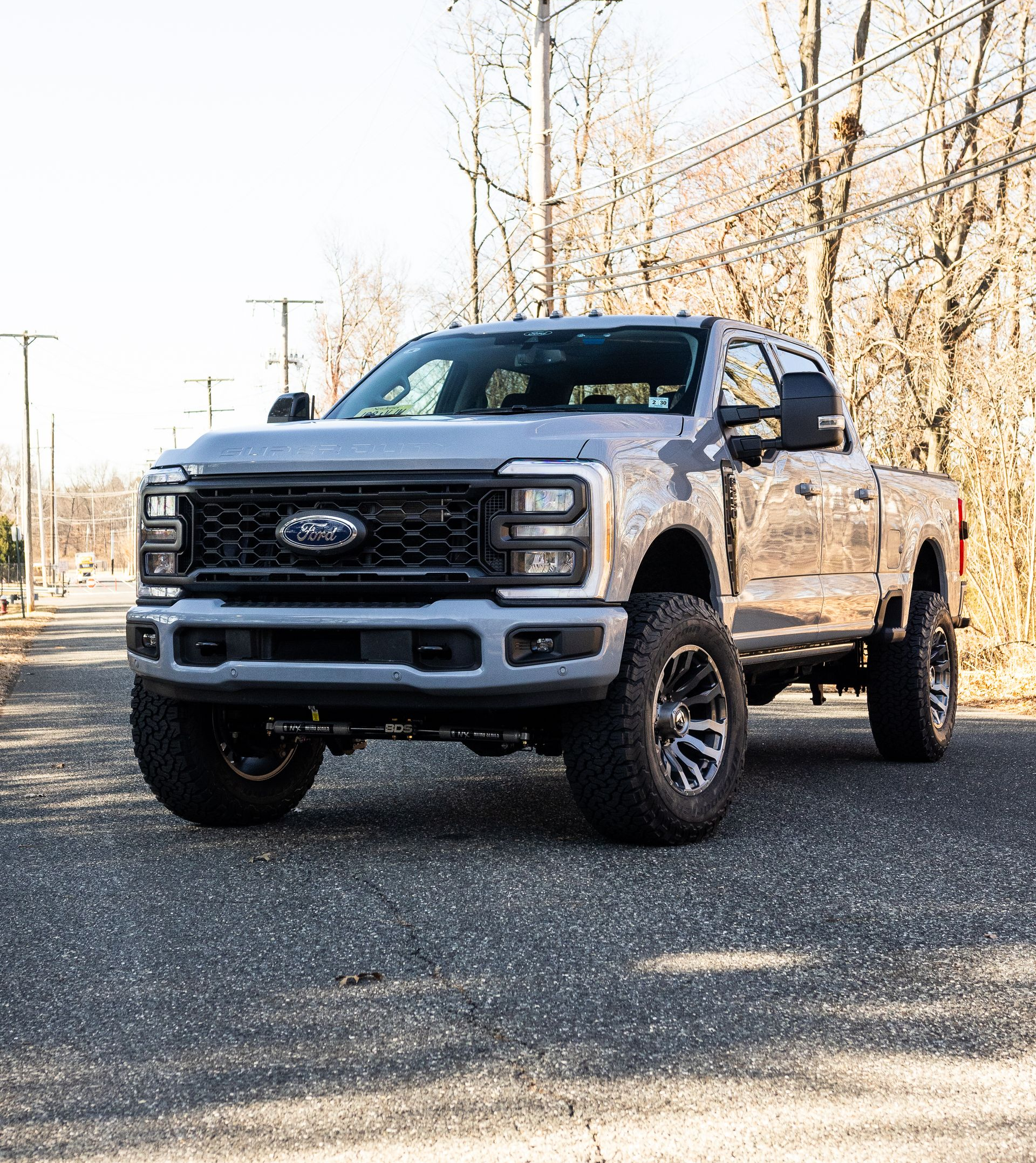 Silver Ford truck, lifted, with black grille and wheels, parked on asphalt.