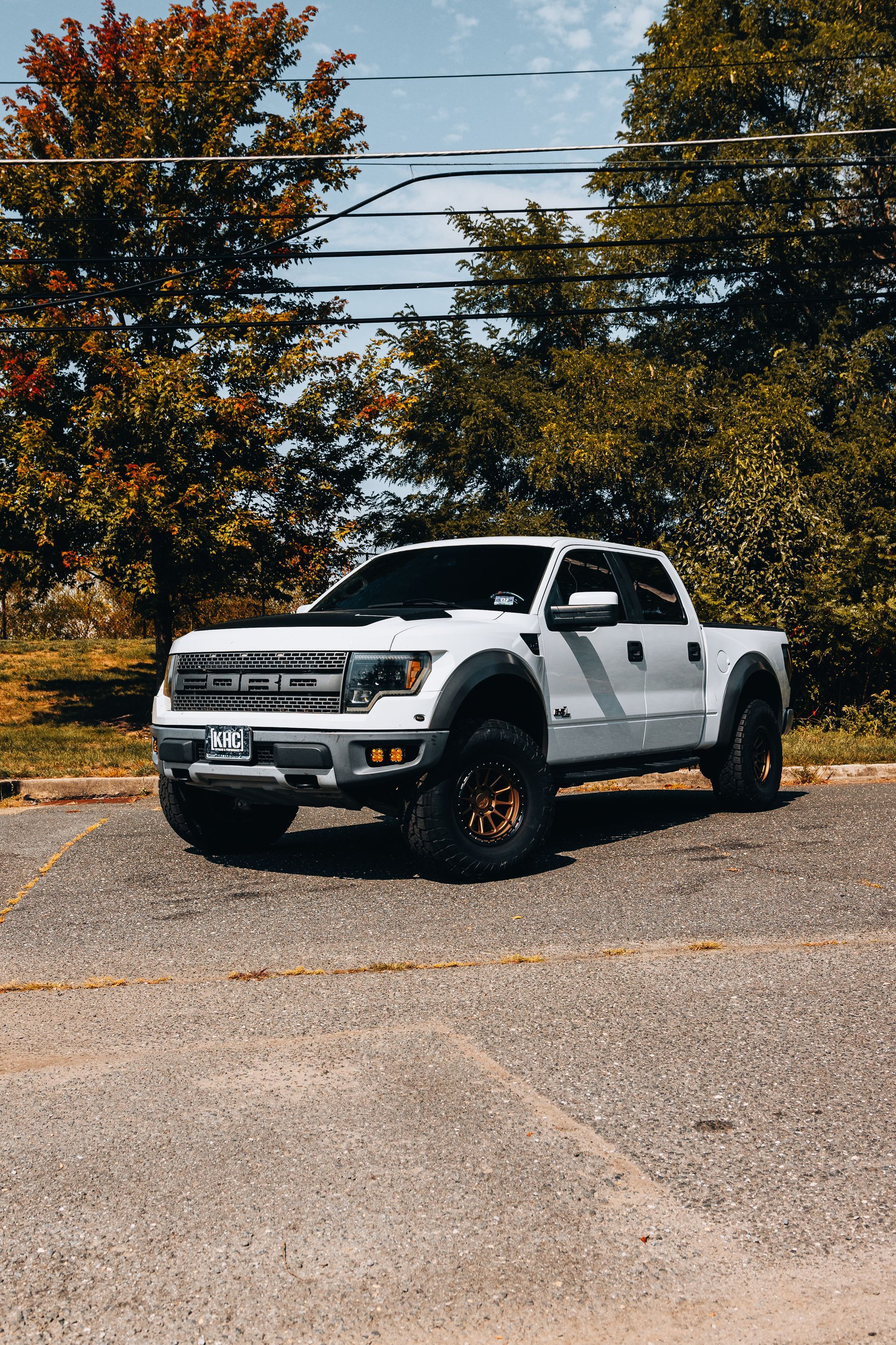 White Ford Raptor pickup truck parked on asphalt, trees in background.
