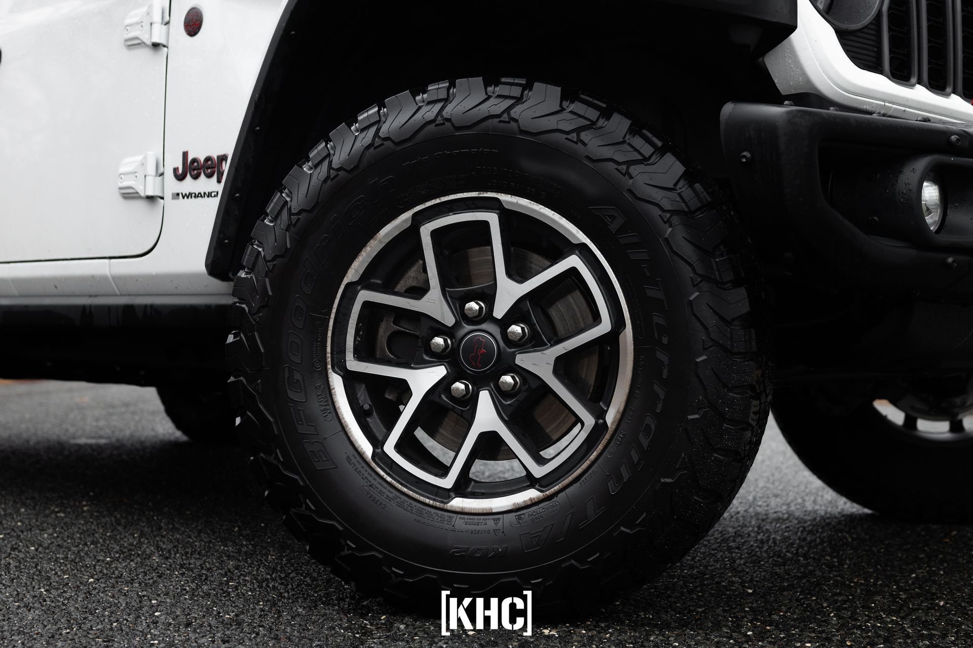 White Jeep SUV tire with black and silver rim on wet pavement.