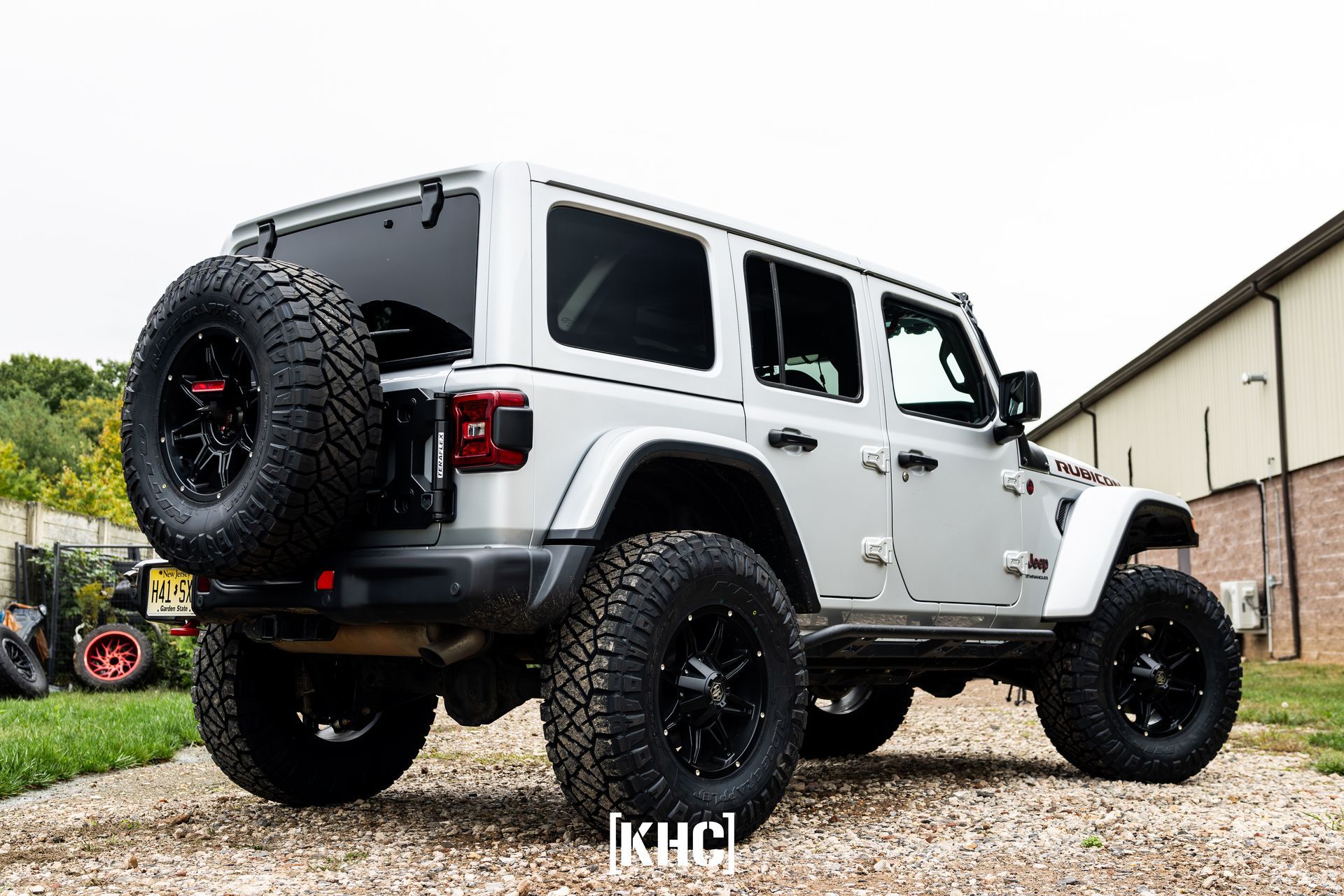 Silver Jeep Wrangler with large black tires parked outside.