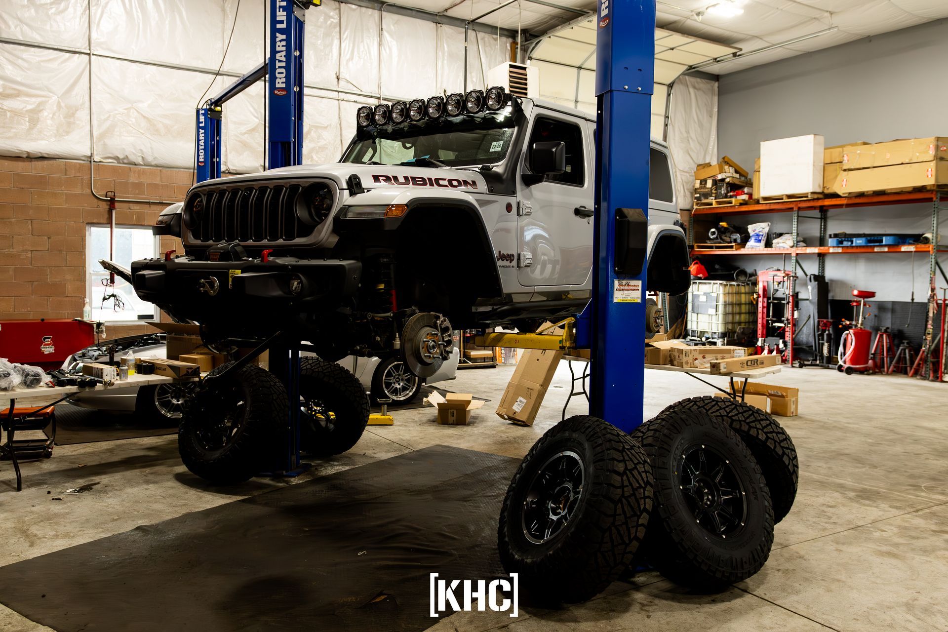 Jeep Gladiator on a lift in a shop, tires removed, awaiting service.