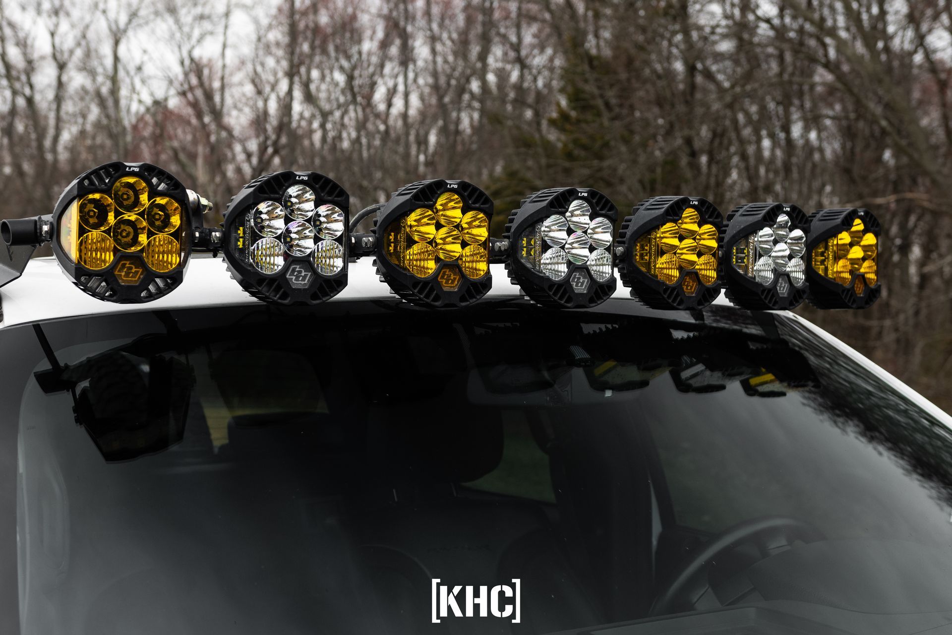 Black vehicle roof with six off-road LED lights. Alternating amber and white lights, daytime setting.