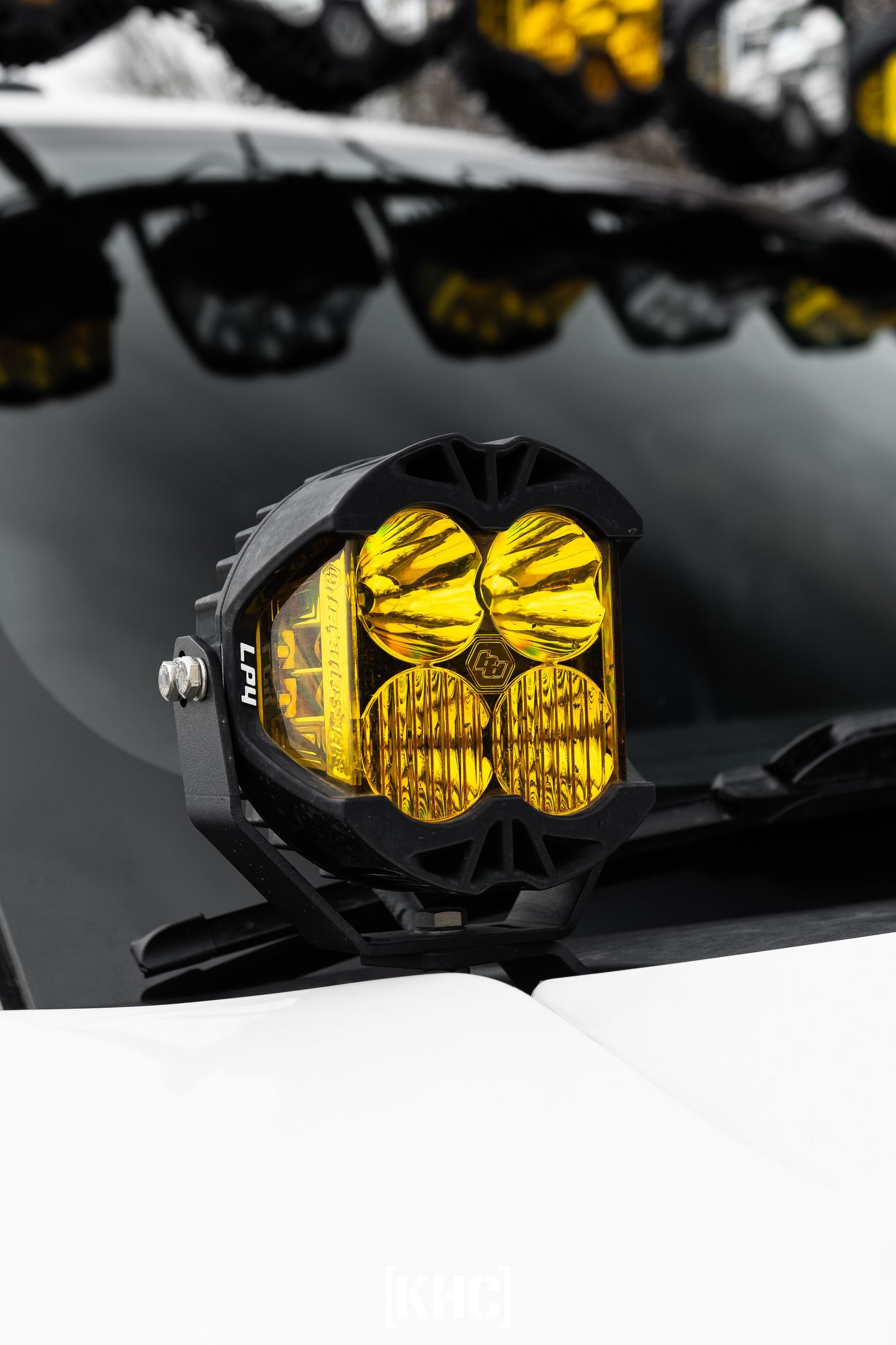 Black off-road light with four yellow lenses mounted on a vehicle.