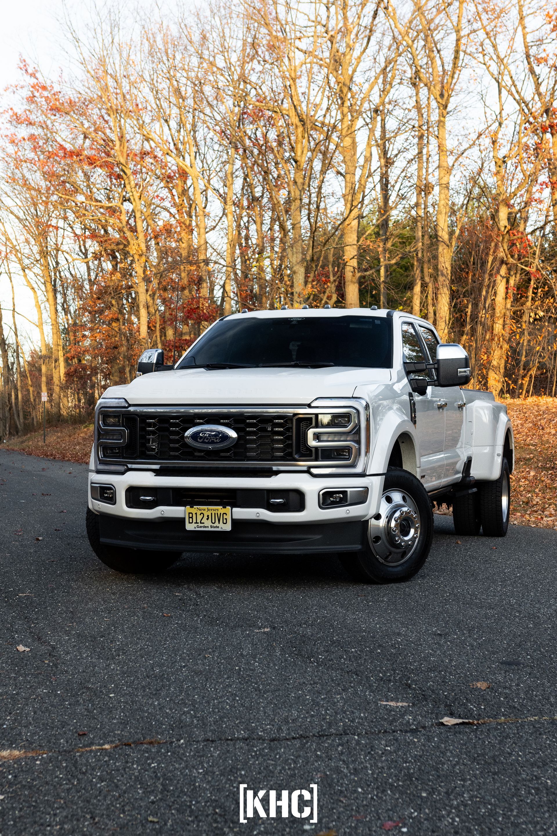 White Ford F-350 dually pickup truck parked on a paved road with trees in the background.