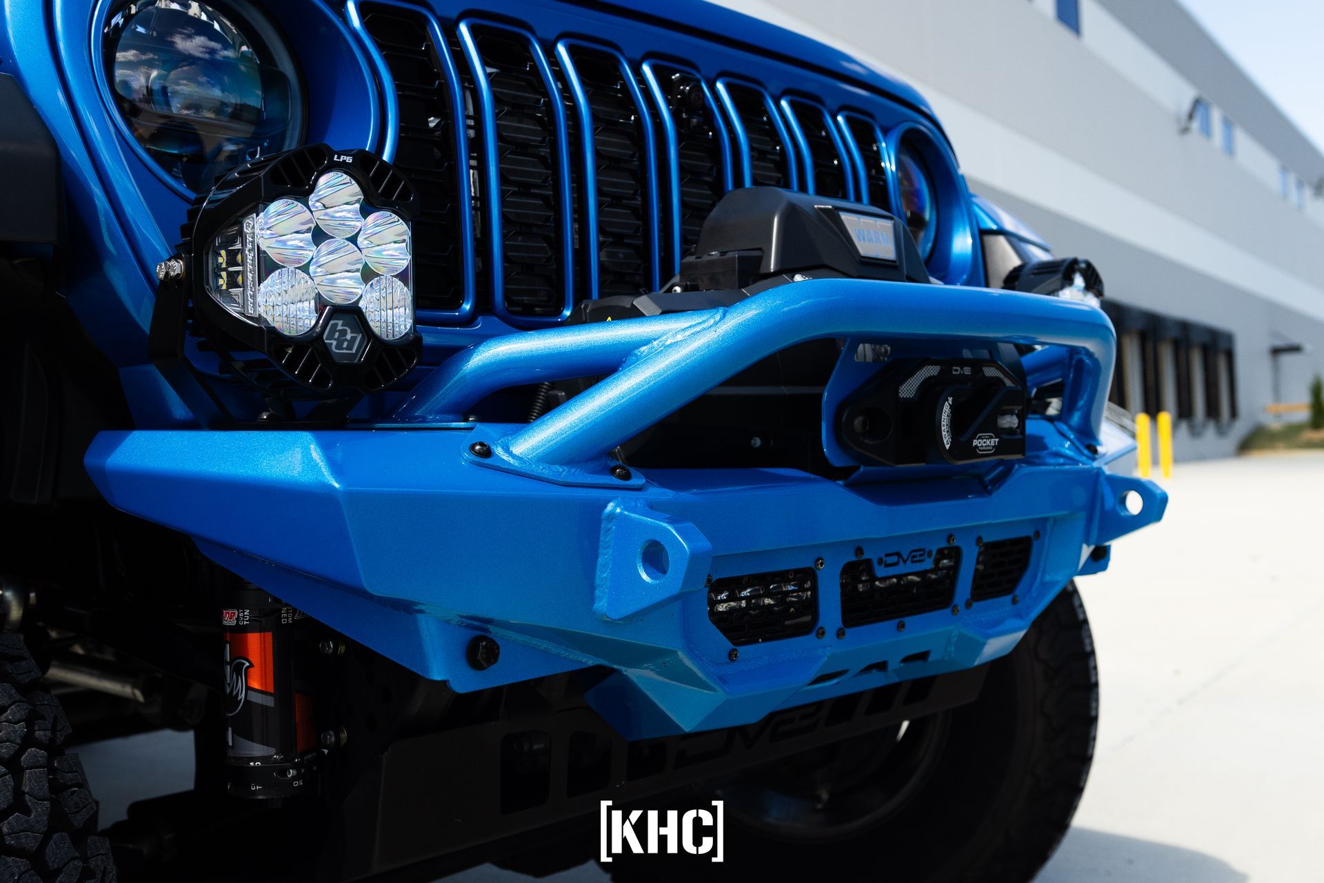 Blue Jeep Wrangler with custom bumper, grill, and lights, parked outside.