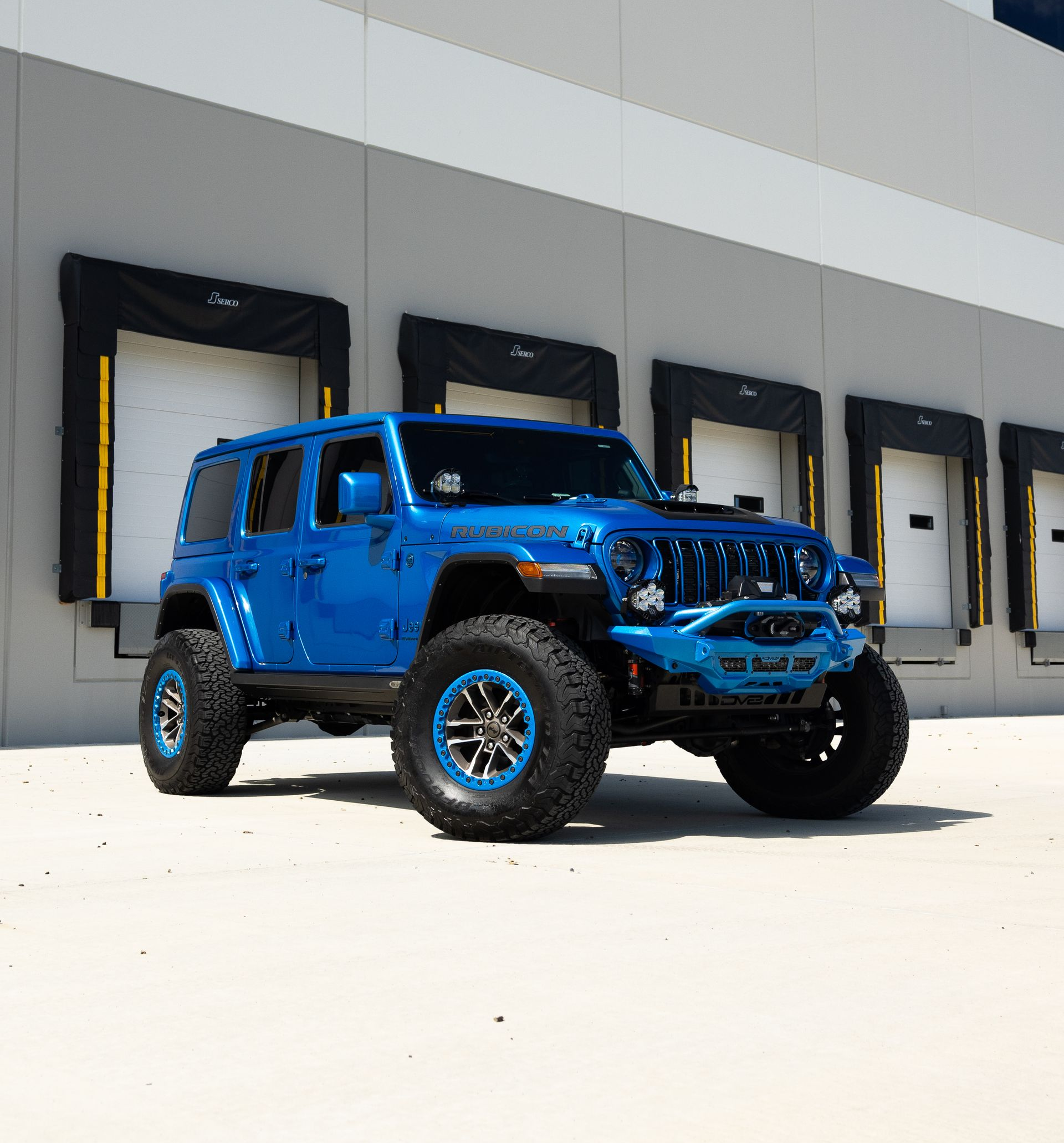Blue lifted Jeep Wrangler Rubicon parked in front of loading docks.