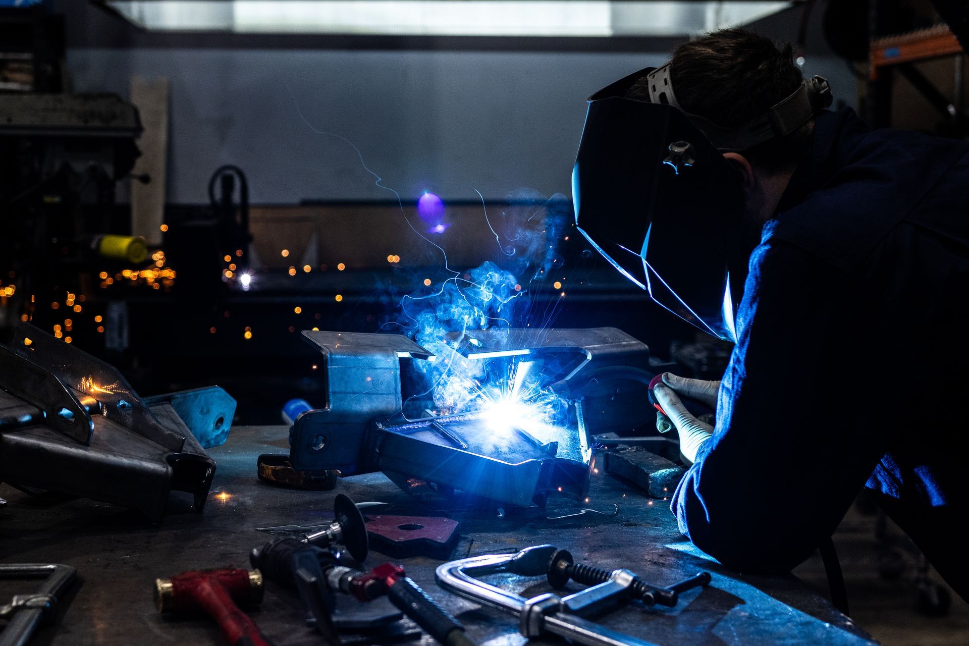 Welder in a workshop, sparks flying, welding metal on a workbench.