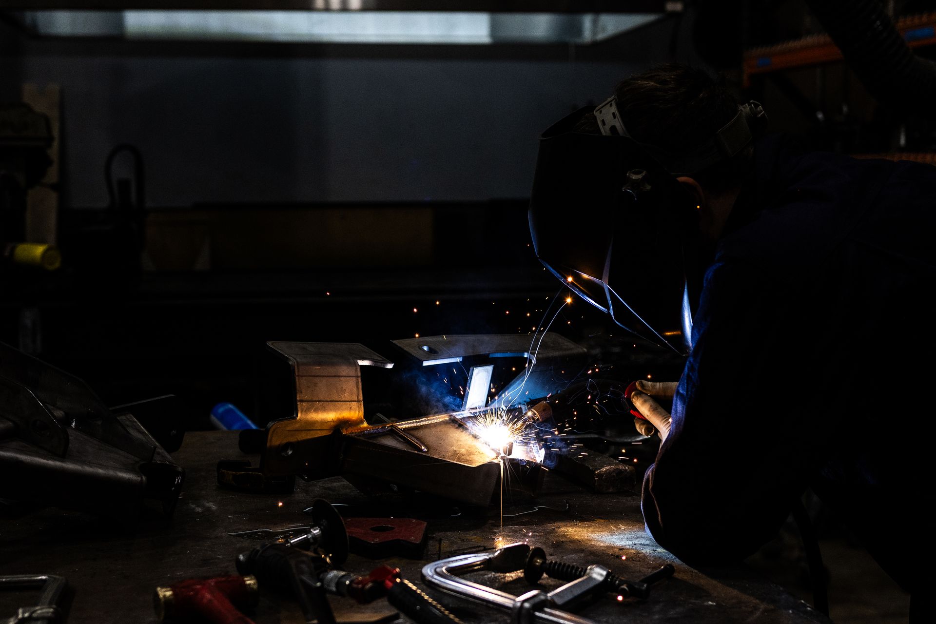 Welder in a workshop, welding metal; sparks flying.
