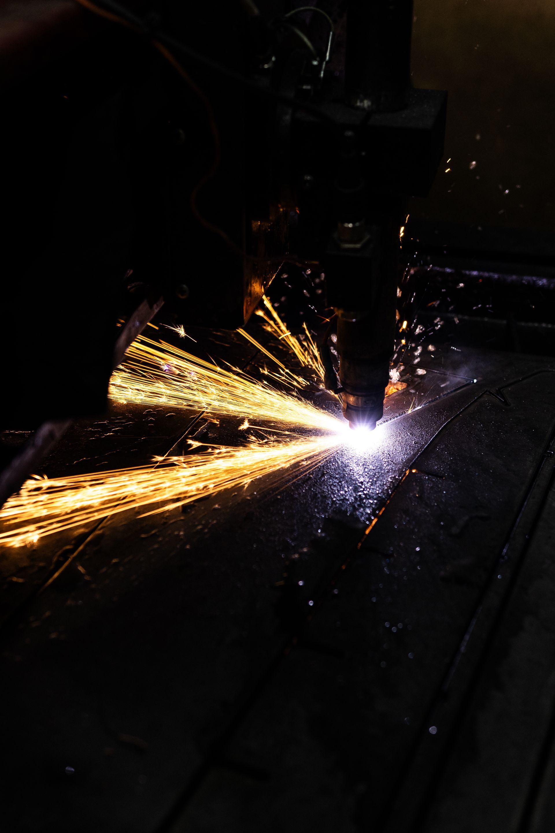 Bright sparks fly from a cutting tool welding dark metal in a dim workshop.