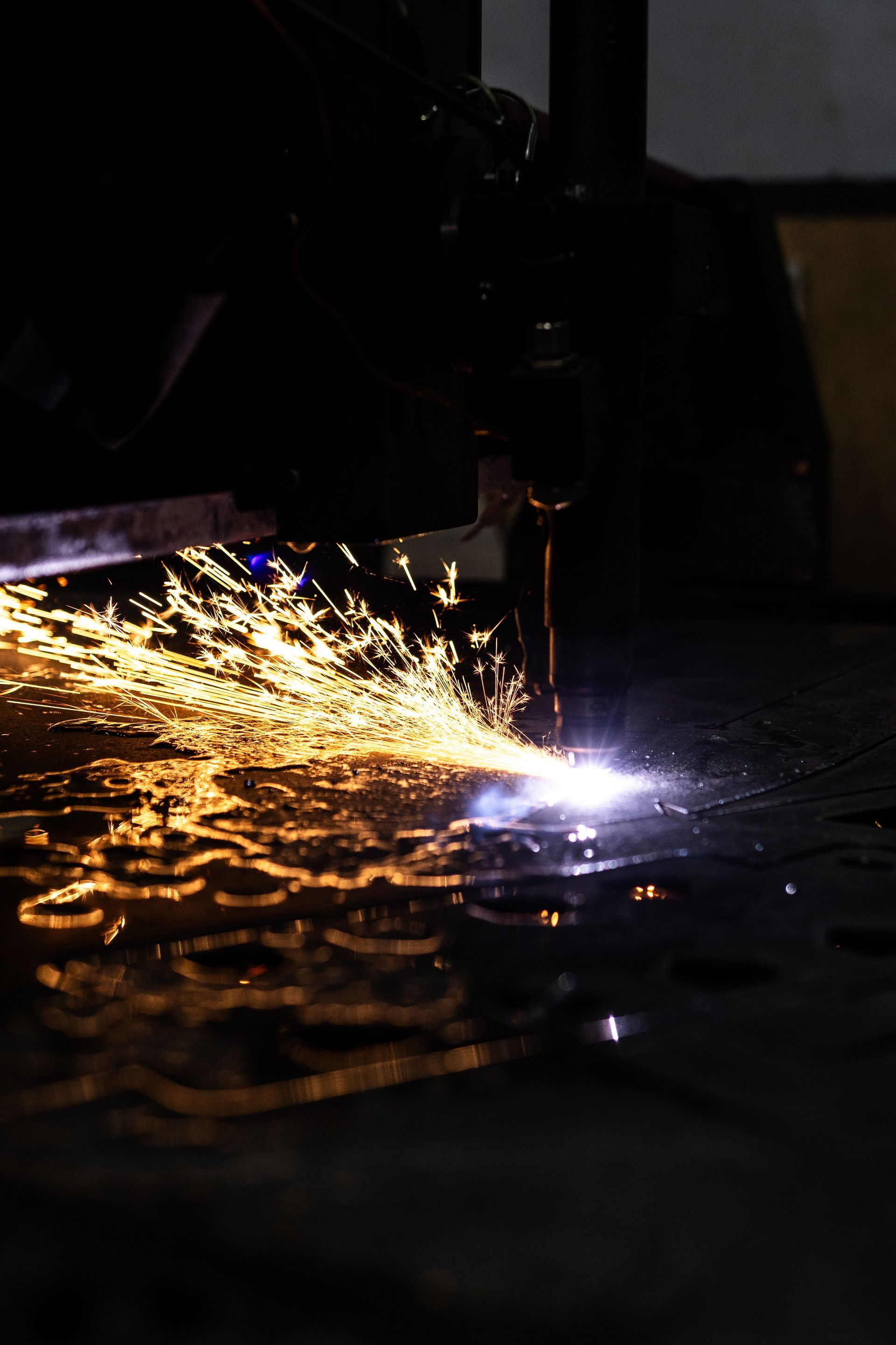 Sparks erupt from a plasma cutter as it shapes metal; dark industrial setting.