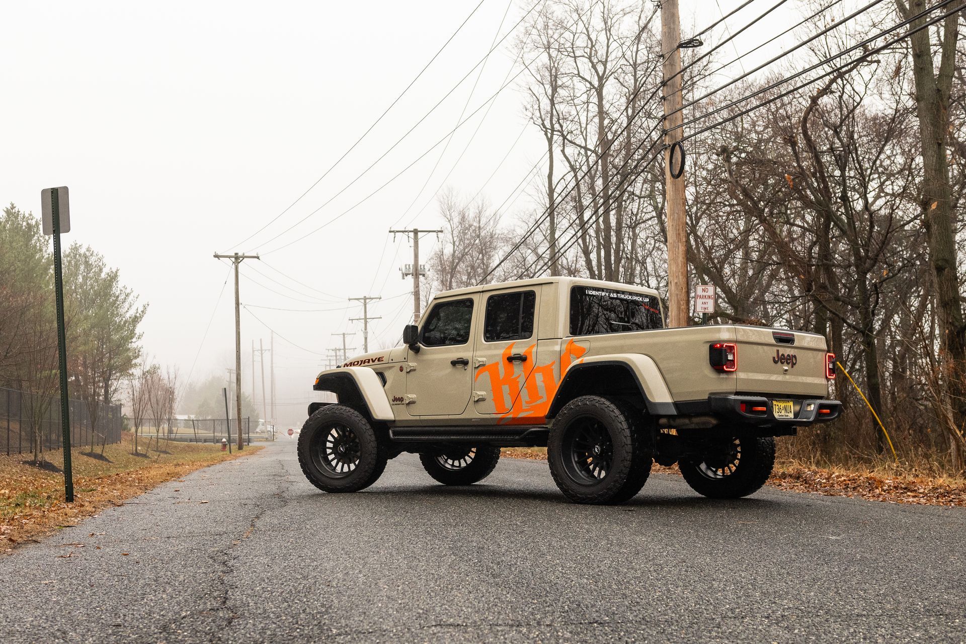Tan Jeep Gladiator truck with orange design on the side, parked on a wet road, misty background.
