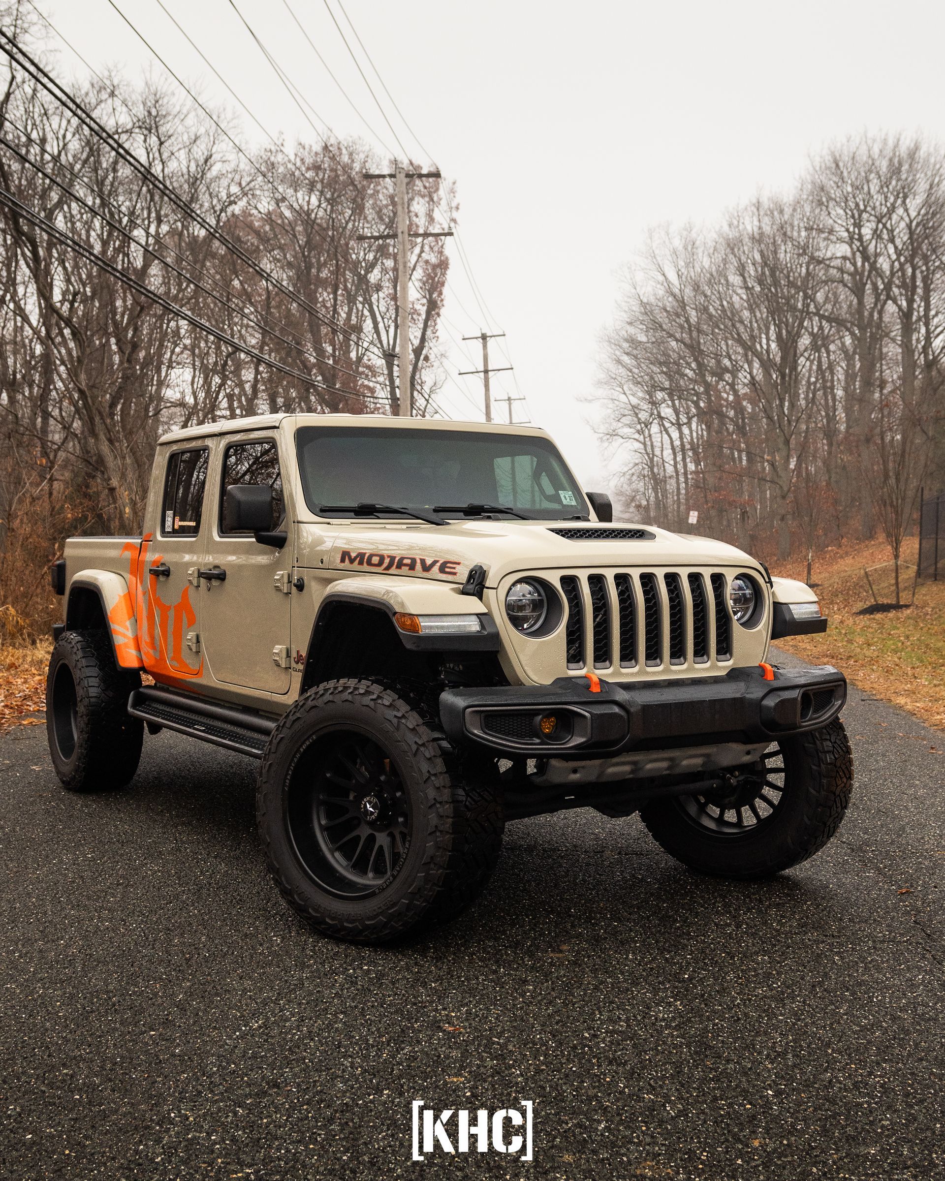 Tan Jeep Gladiator truck with black wheels and orange accents parked on a paved road.