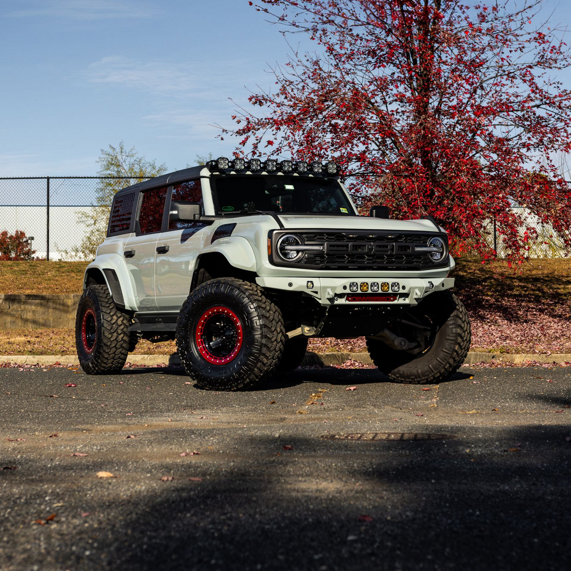 Gray Ford Raptor truck, front view, with blue FORD lettering on grille, outdoors, autumn setting.