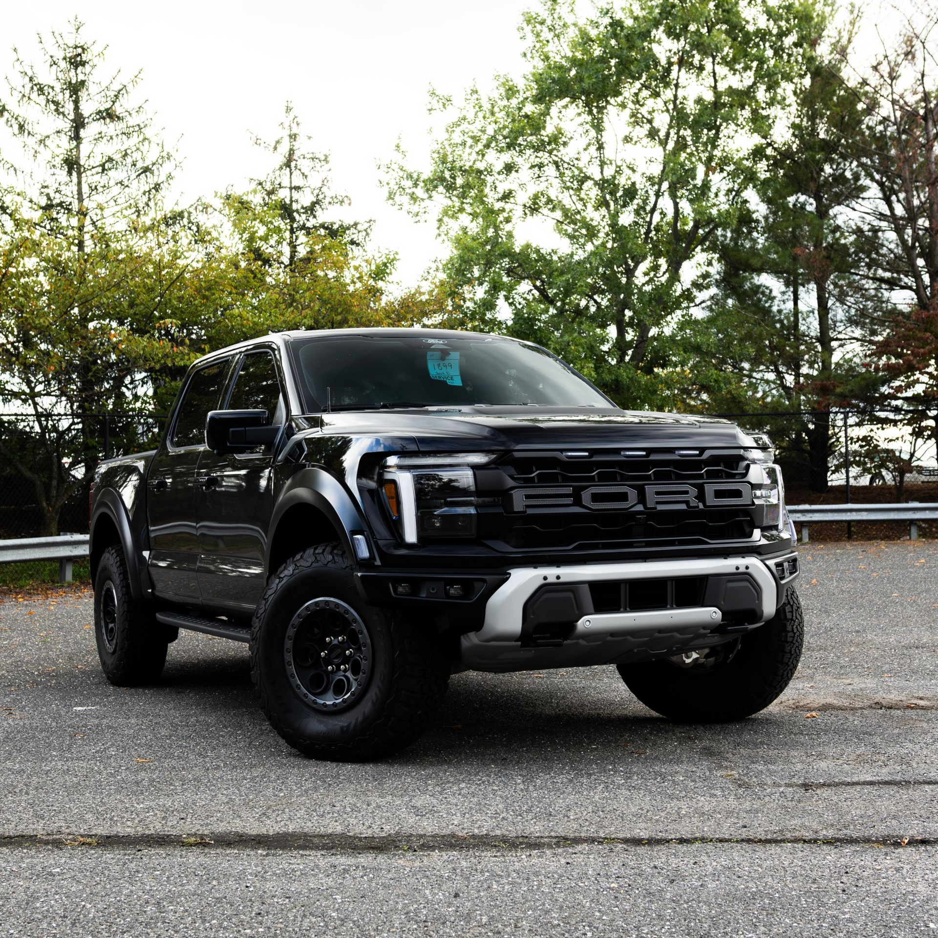 White lifted Ford F-150 truck with custom grille and wheels parked on a road, trees in the background.