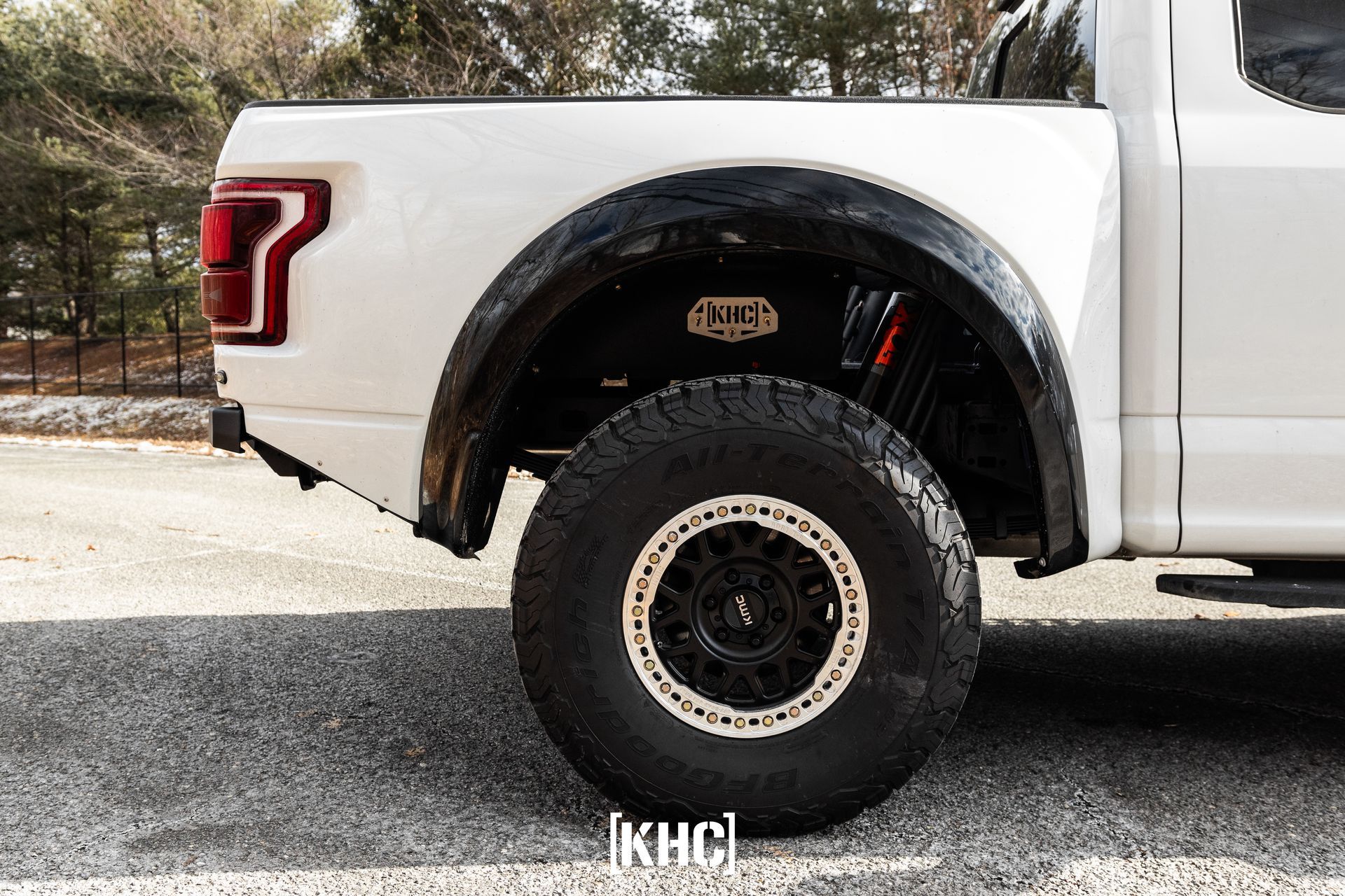 White Ford truck with black fender flares, large off-road tire, and red suspension.