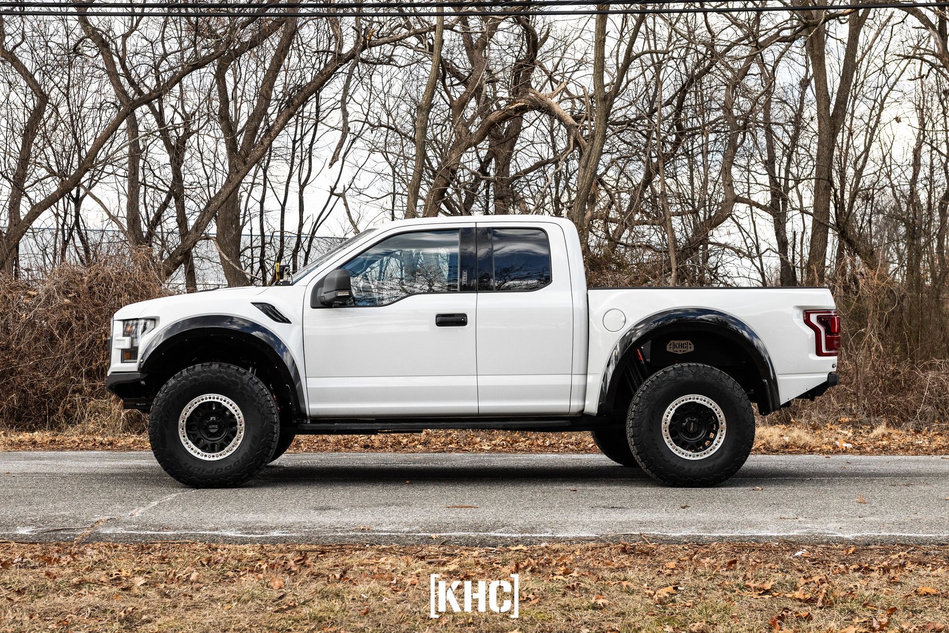 White Ford Raptor pickup truck on a paved road with trees in the background.
