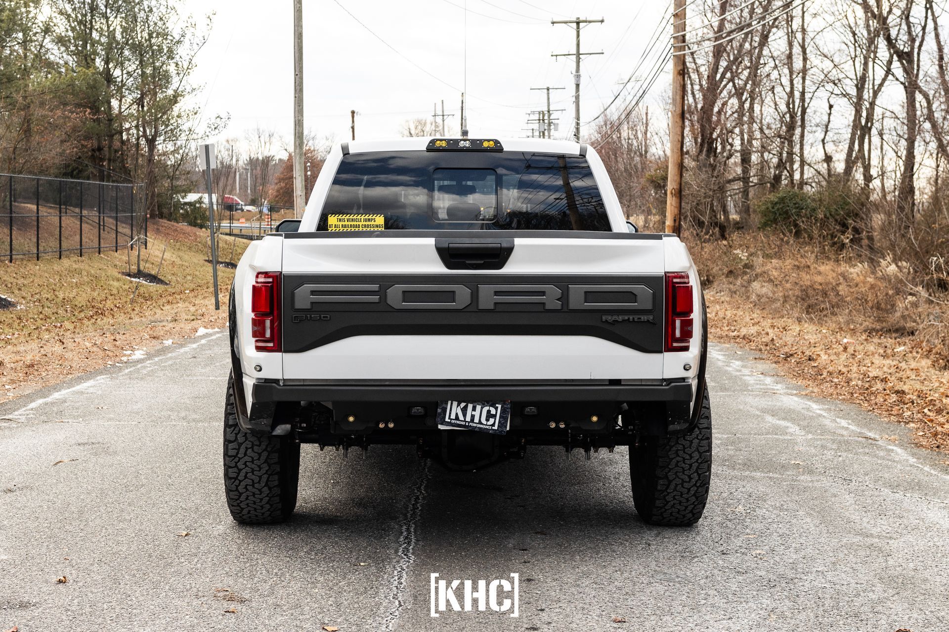 White Ford Raptor truck on a paved road, rear view. Black 