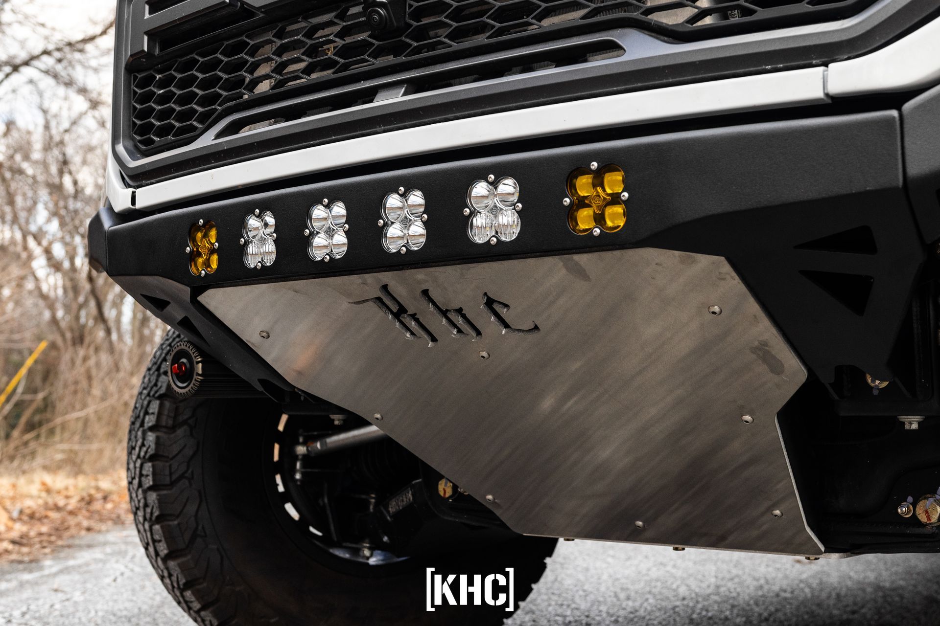 Close-up of a truck's front bumper with off-road lights and a metal skid plate.