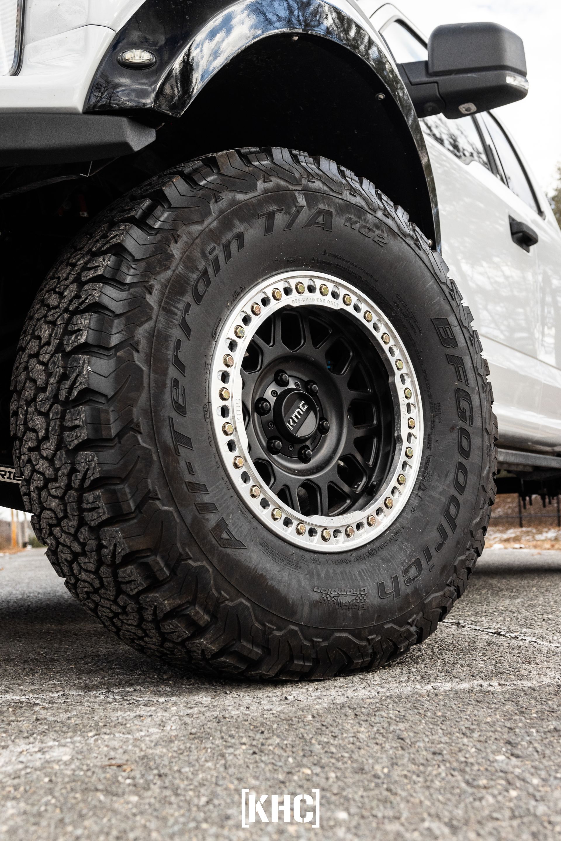 Close-up of a large black off-road tire on a white truck. Tire has a silver rim and black center cap.