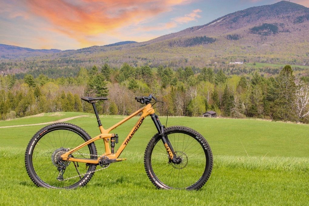 Yellow Transition Sentinel mountain bike in a field with Burke Mountain, Vermont in the background