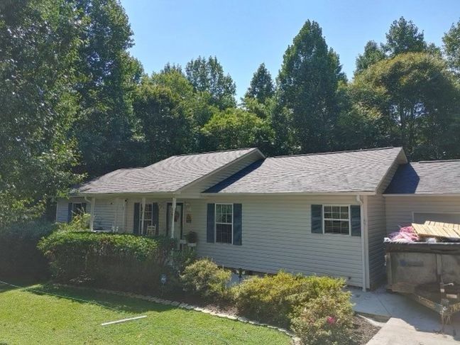 a white house with a gray roof is surrounded by trees Birds Eye Roofing Group.