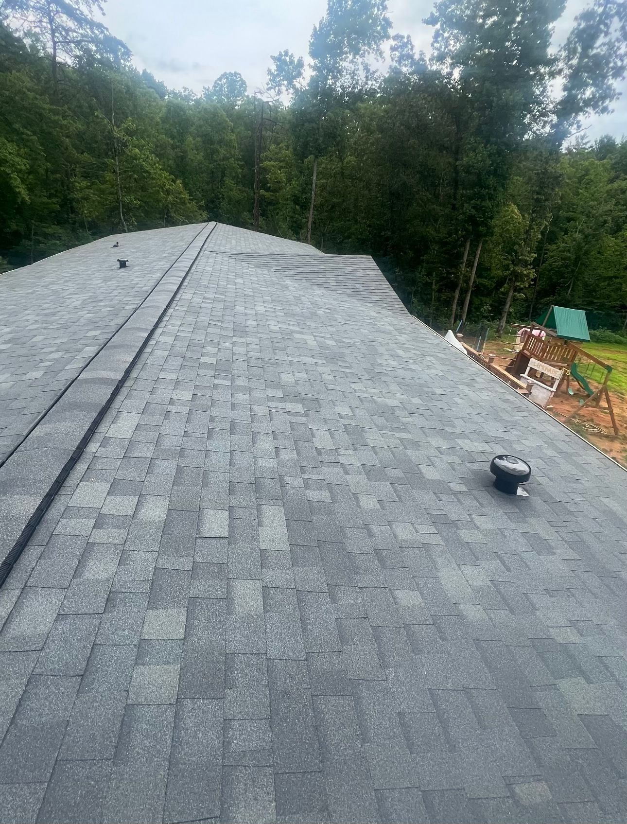 a roof with a lot of shingles on it is surrounded by trees Birds Eye Roofing Group.