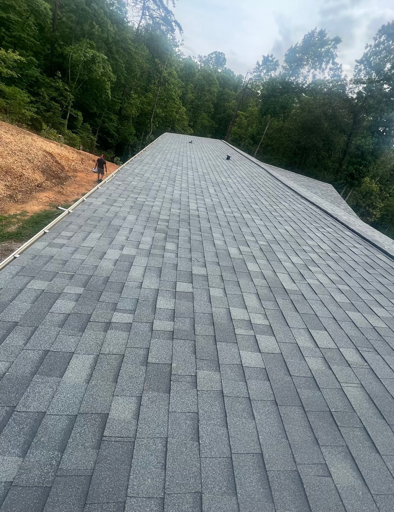 a roof with a lot of shingles on it is surrounded by trees Birds Eye Roofing Group.