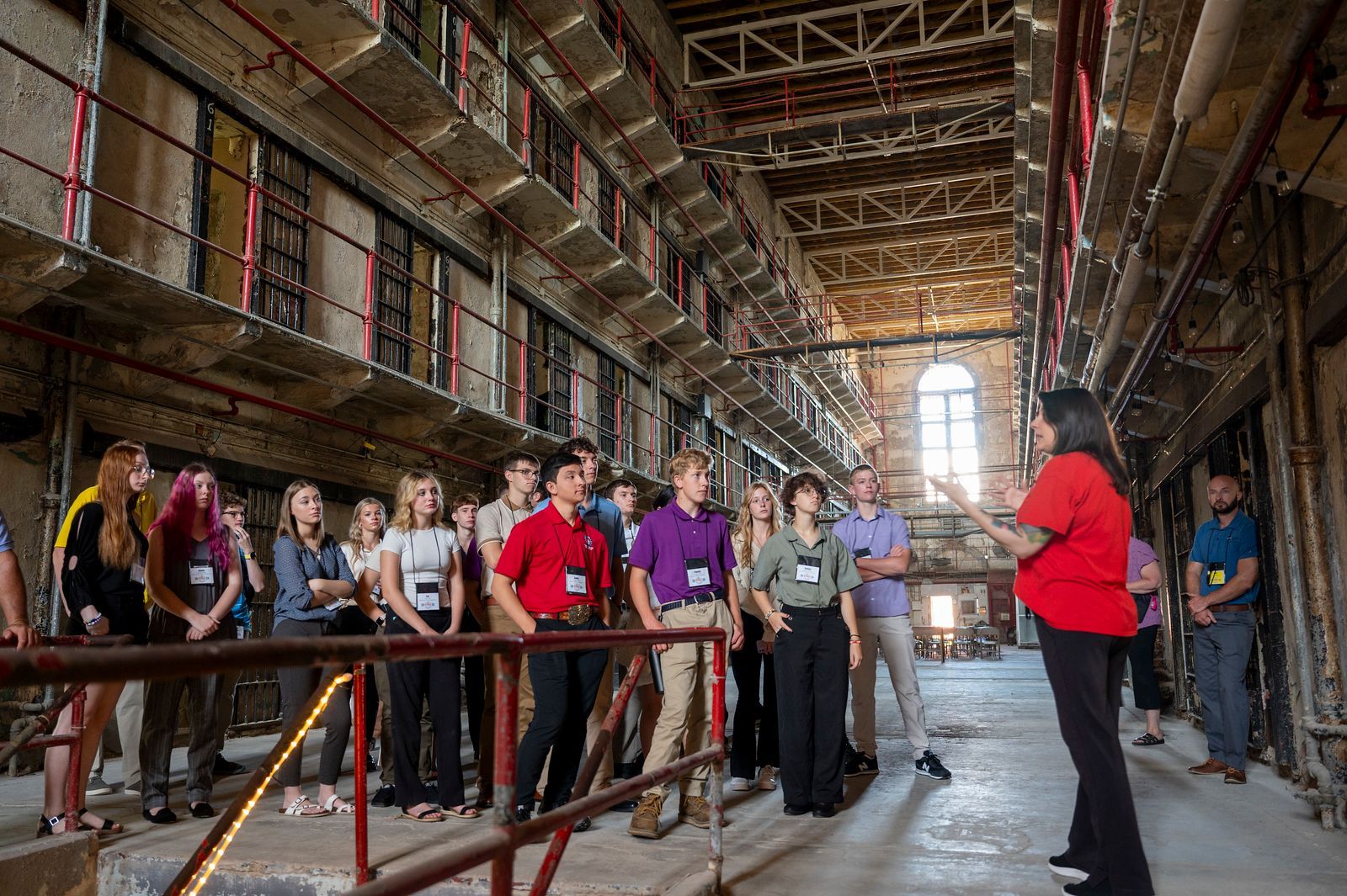 A woman in a red shirt is giving a tour of a building to a group of people.