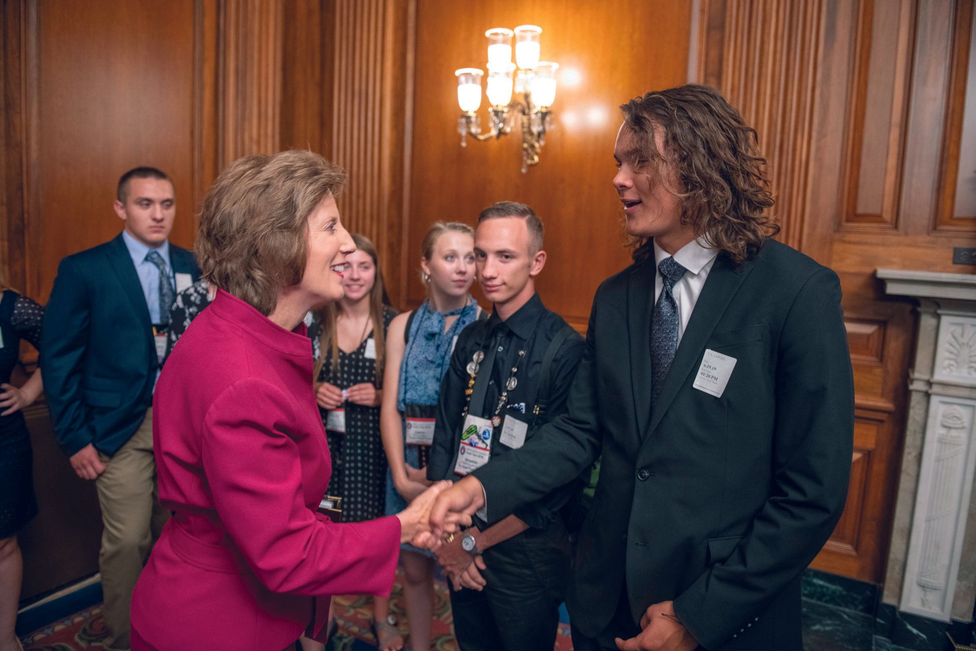 A woman in a pink jacket is shaking hands with a young man in a suit.