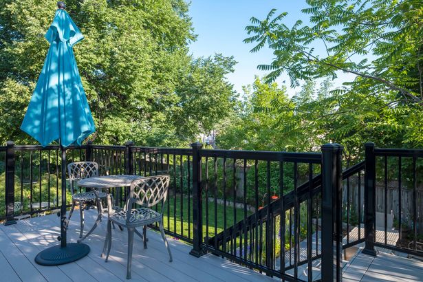 Patio deck with a closed blue umbrella, metal table and chairs, and black railing overlooking trees