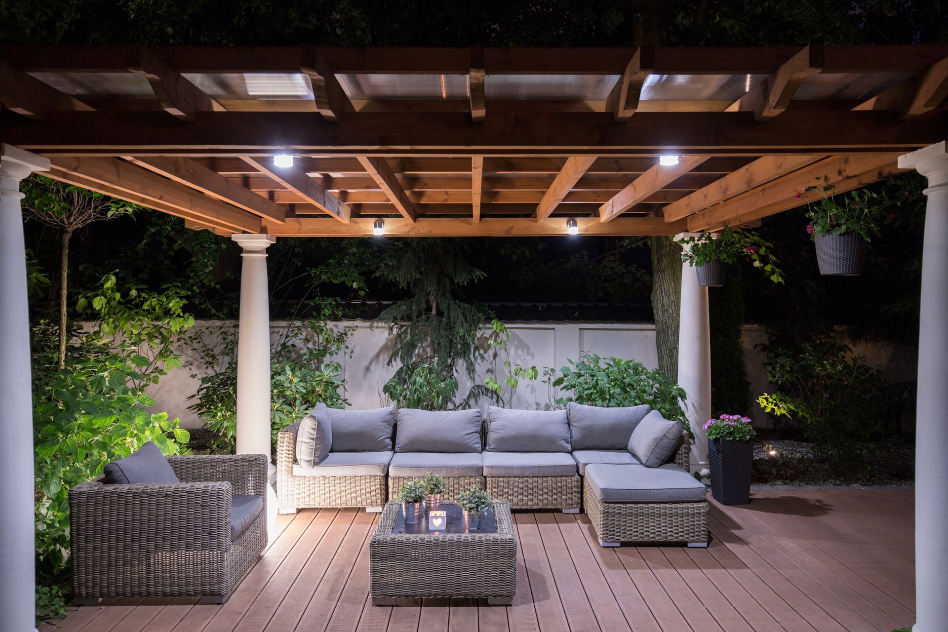 Covered patio with gray outdoor sofa and wicker chairs around a coffee table, lit by warm string lights at night