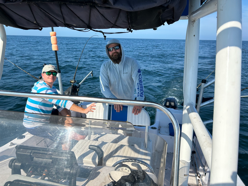 Two people smiling on a boat on the open ocean. They are wearing casual clothing and sunglasses.