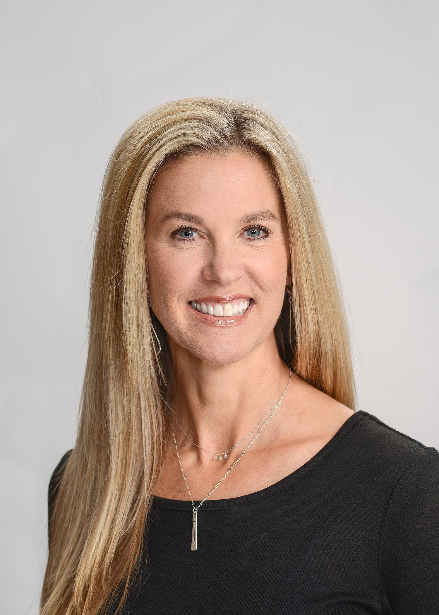 A woman with long blonde hair is wearing a black shirt and smiling.