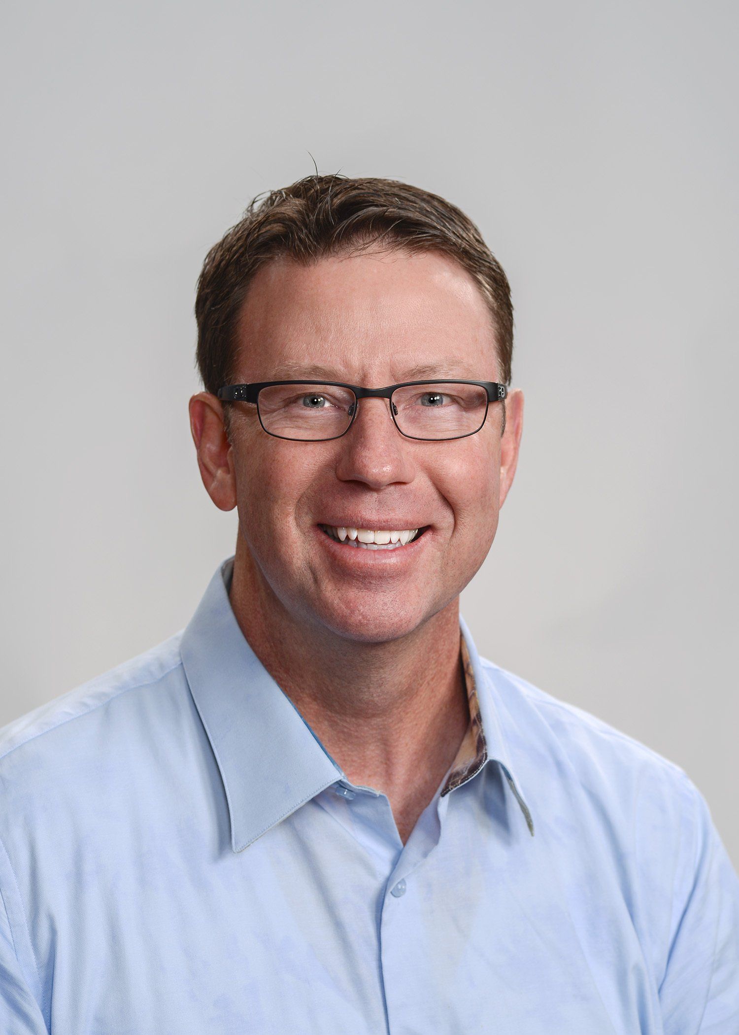 A man wearing glasses and a blue shirt is smiling for the camera.