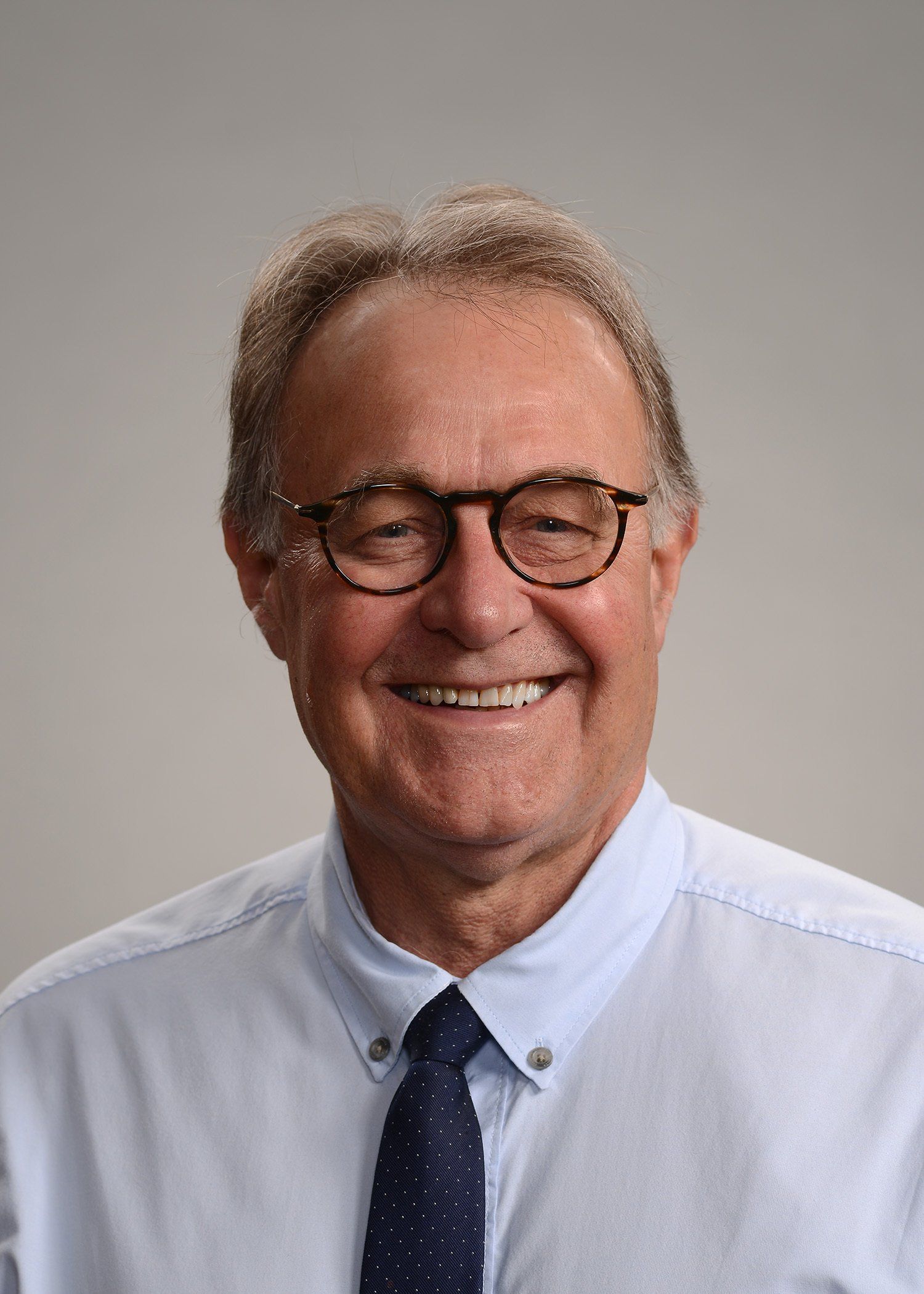 A man wearing glasses and a tie is smiling for the camera.