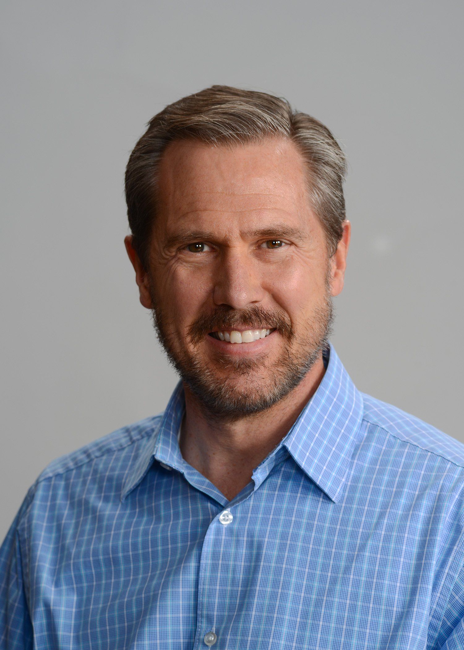 A man with a beard is wearing a blue shirt and smiling for the camera.