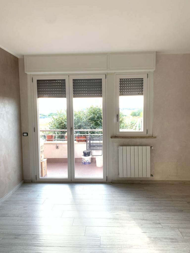 Stanza vuota con pavimento piastrellato, doppie porte bianche che danno su un balcone e un termosifone sulla destra.