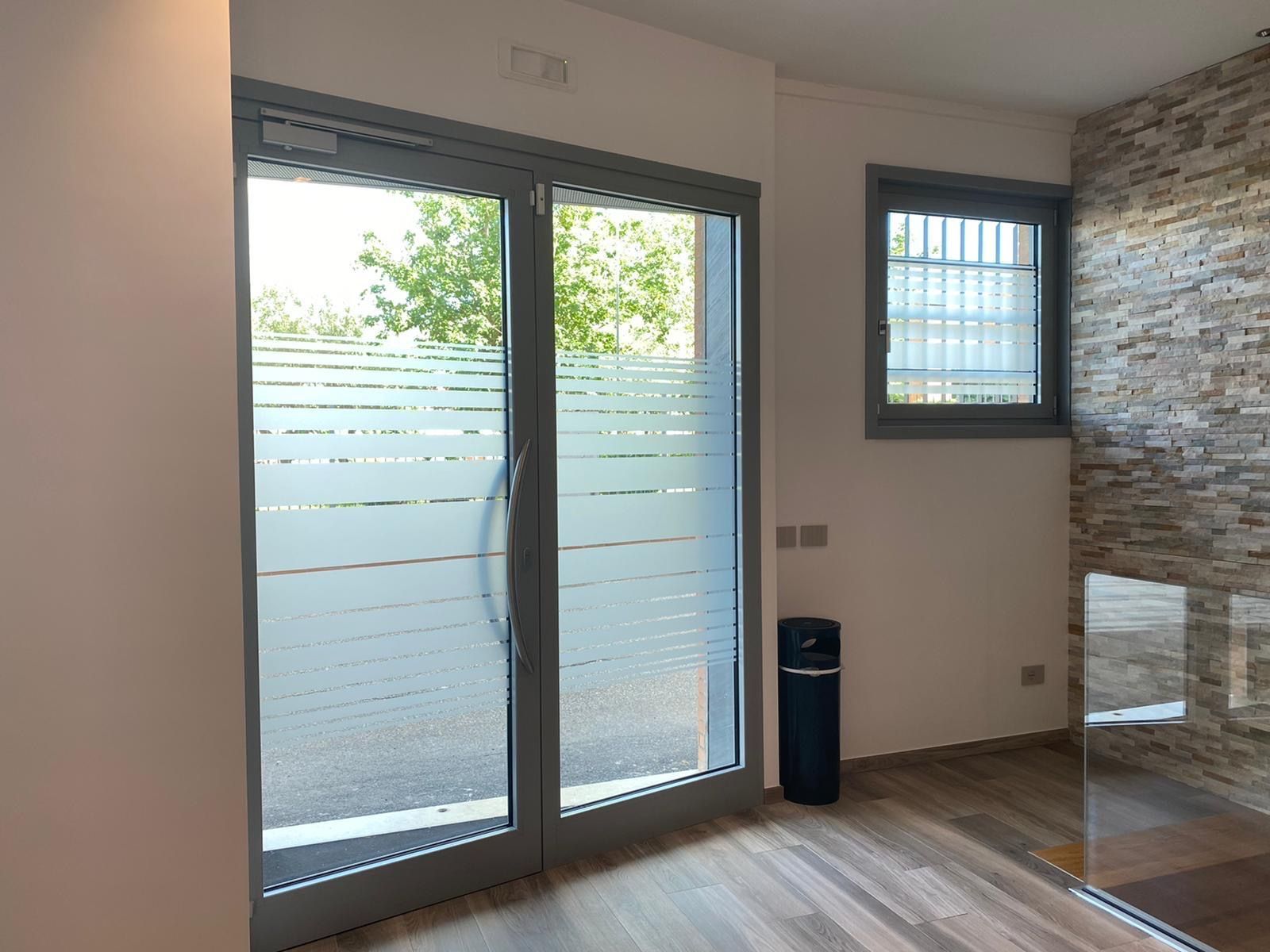Luminosa stanza vuota con porte scorrevoli in vetro, vetri inferiori satinati, pavimento in legno e parete decorativa in pietra.