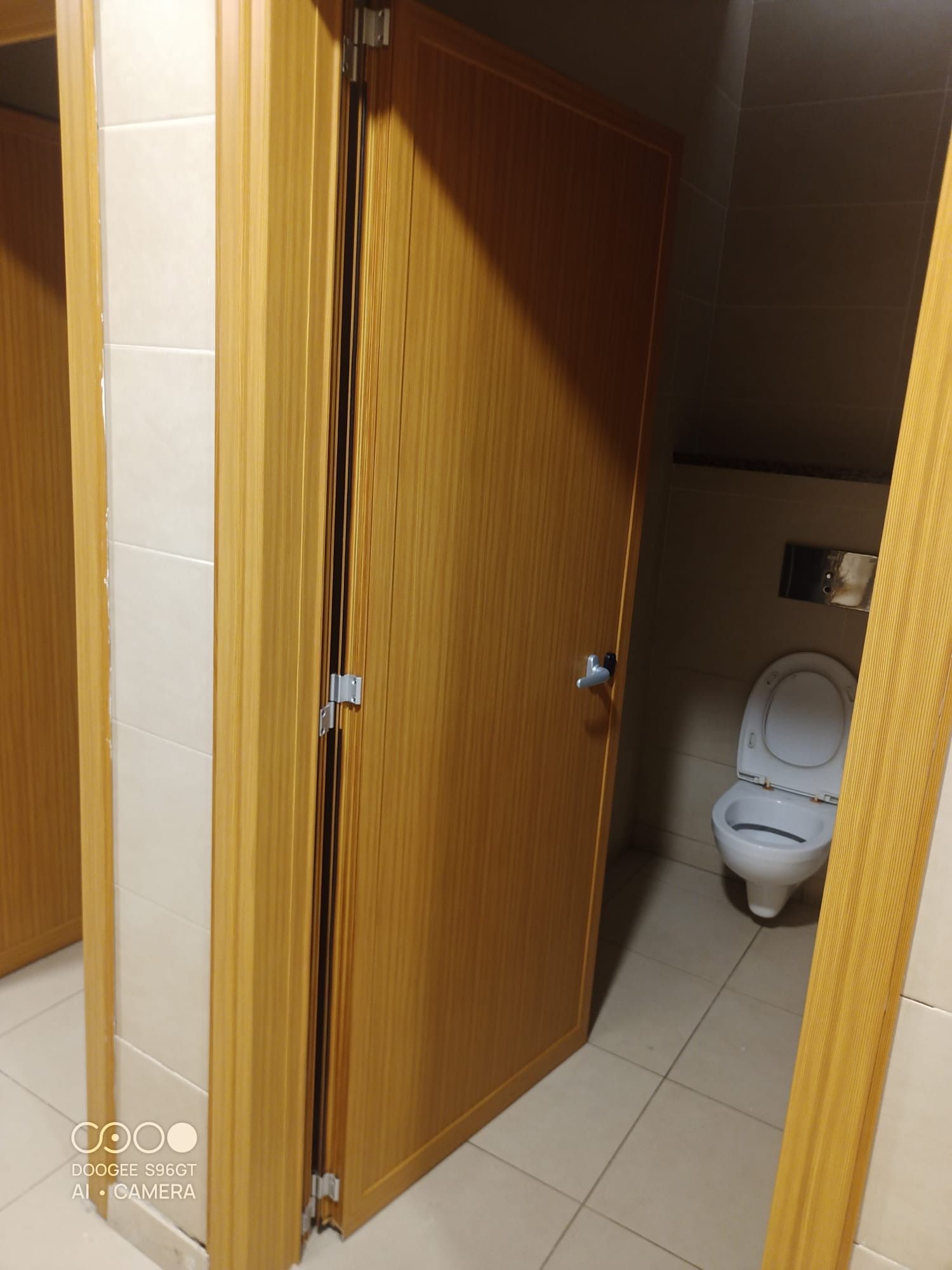 La porta del bagno è aperta e mostra il water all'interno, con pareti e pavimento rivestiti di piastrelle beige.