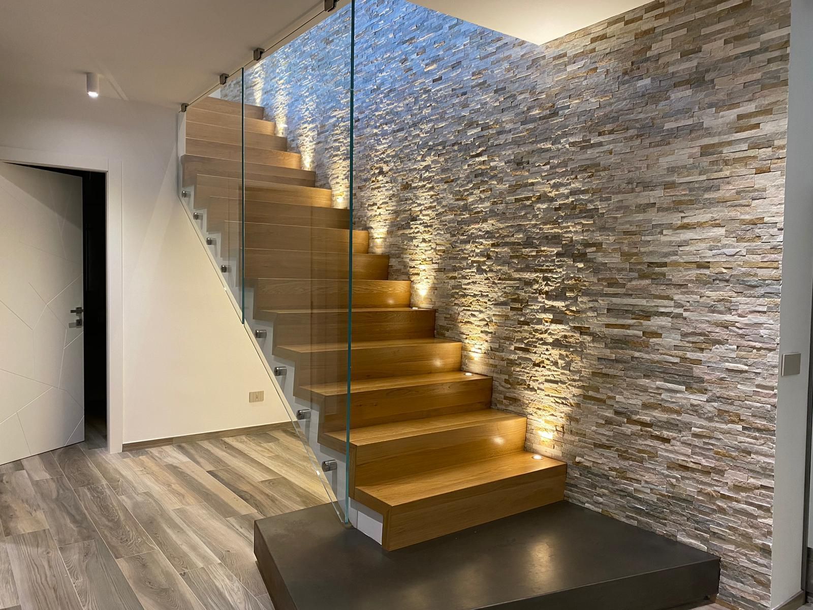 Scala moderna con gradini in legno, ringhiera in vetro e parete decorativa in pietra in un interno minimalista