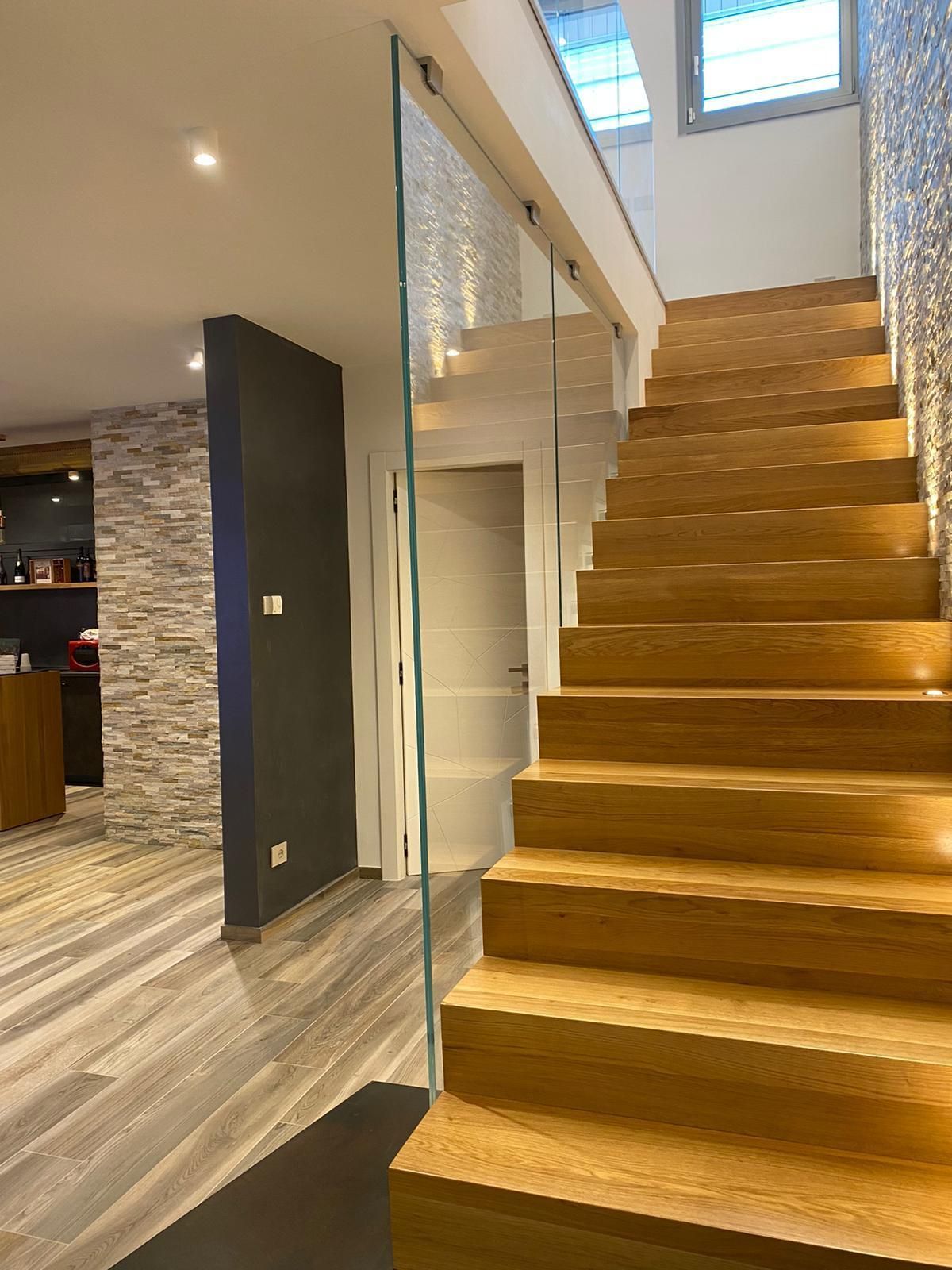 Scala interna moderna con gradini in legno e ringhiera in vetro in un interno residenziale contemporaneo.